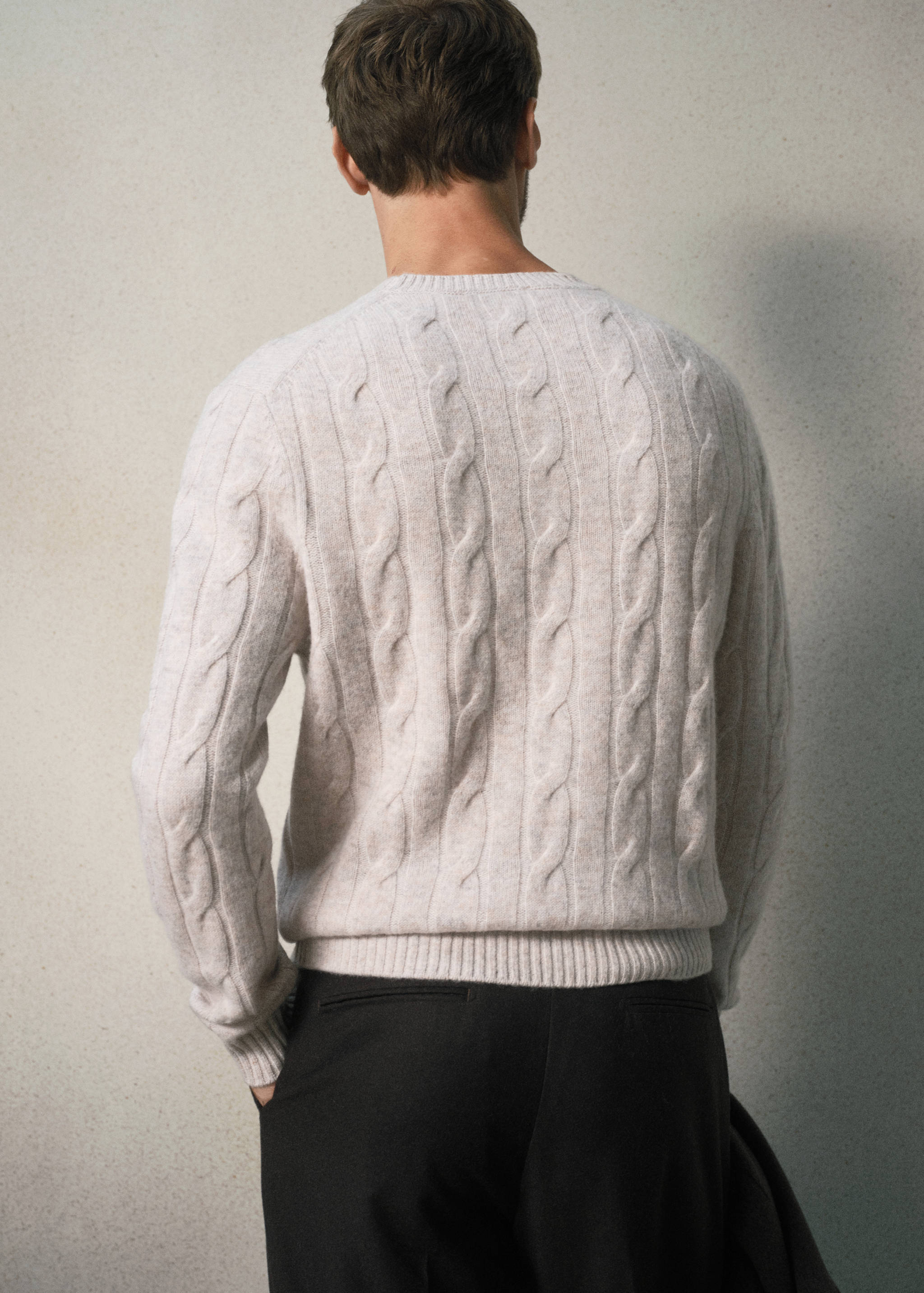 Beige cable-knit sweater with a crew neck, seen from the back.