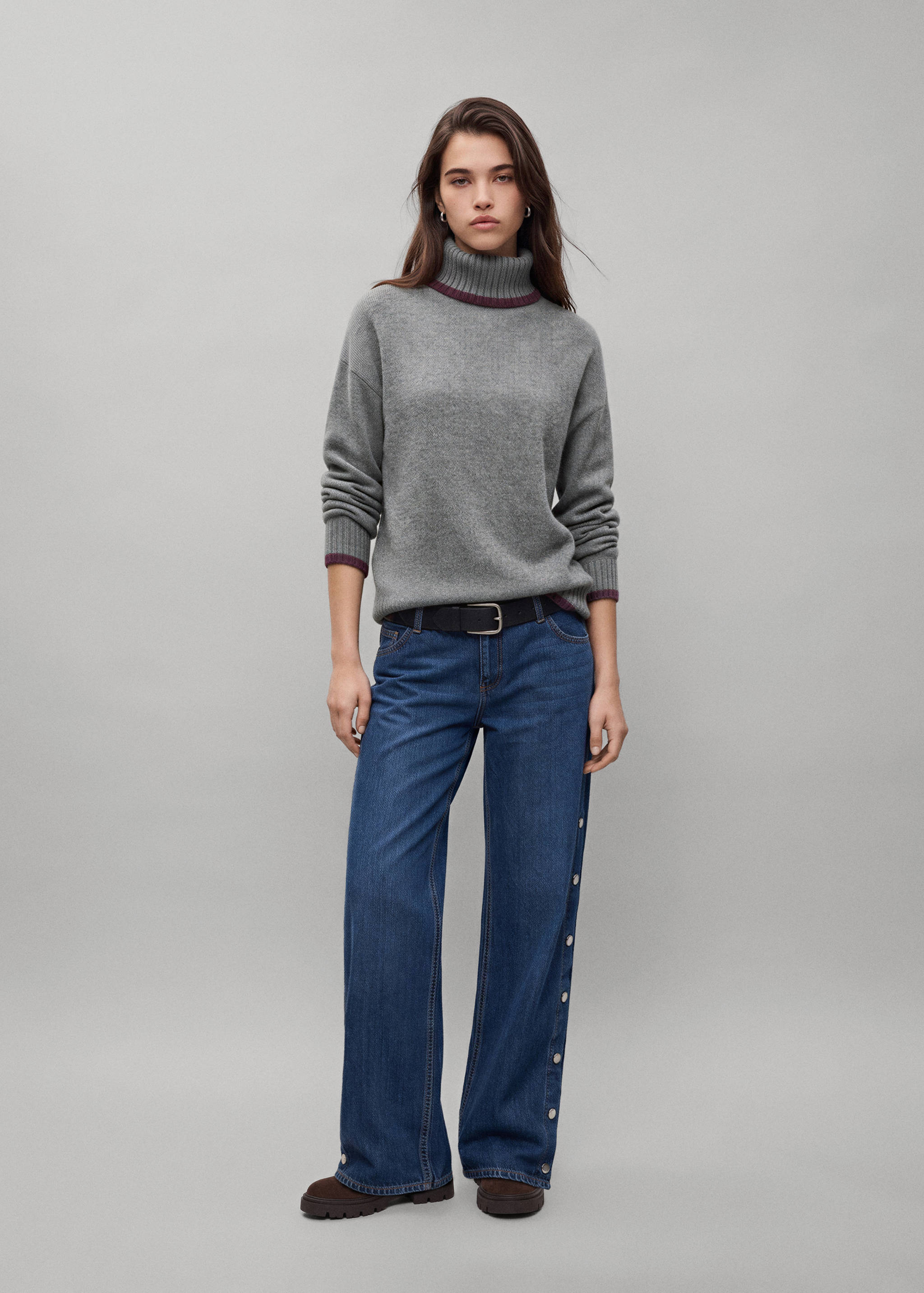 Grey turtleneck jersey with burgundy trim, worn with blue denim trousers.