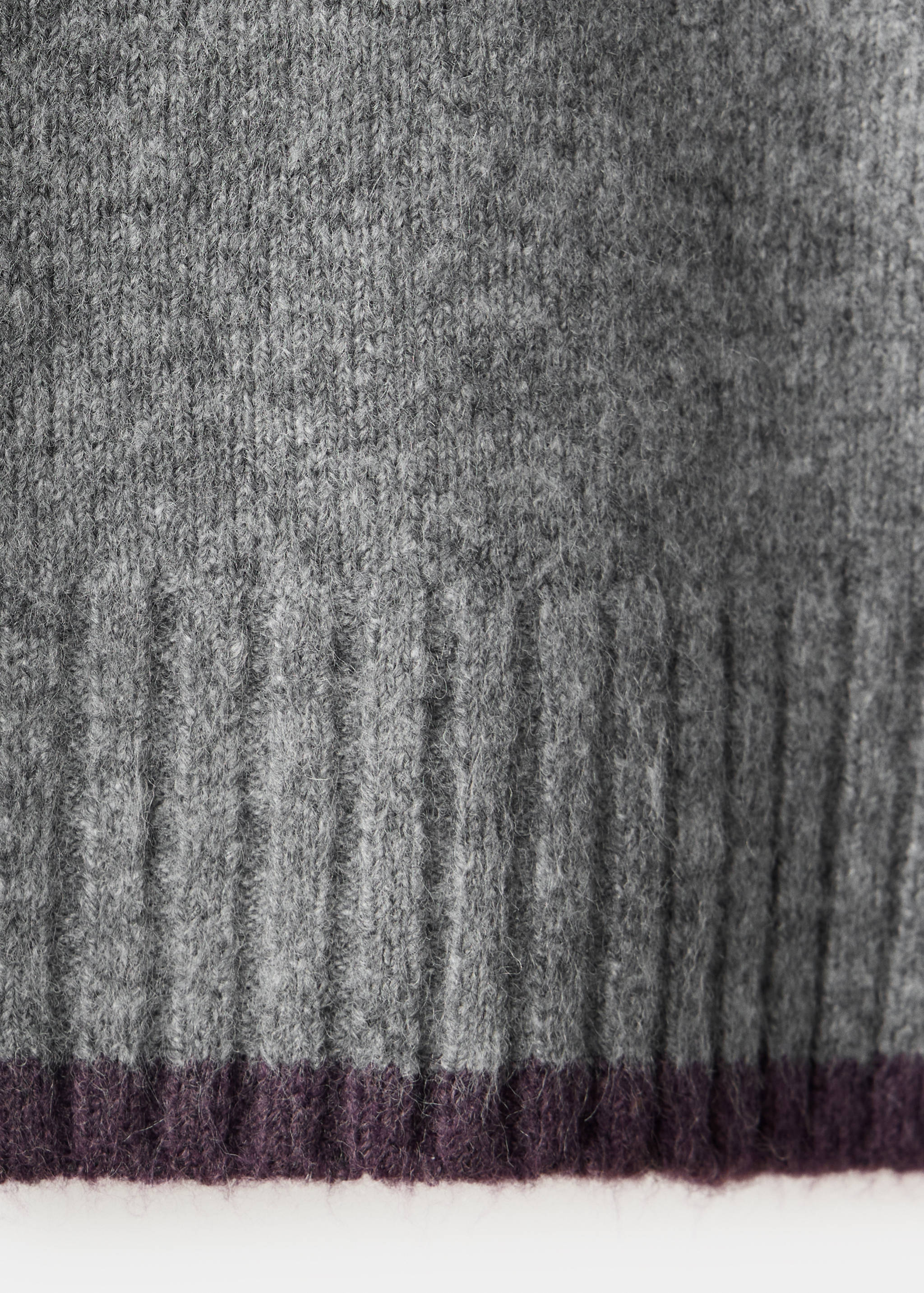 Close-up of a grey fuzzy knit jersey with a ribbed texture and plum hem.