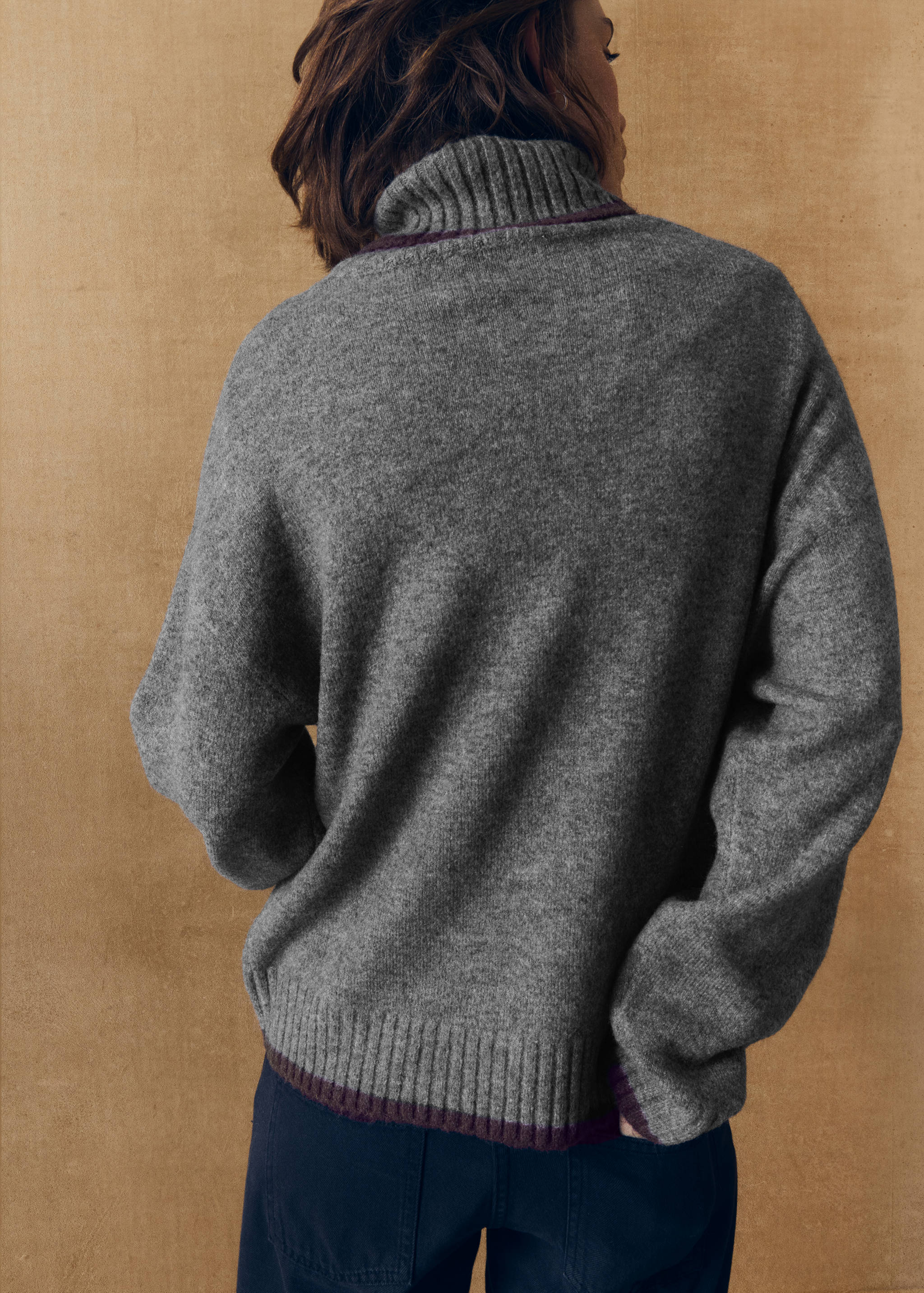 Back view of a grey knit jersey with a high turtleneck and contrasting purple trim.
