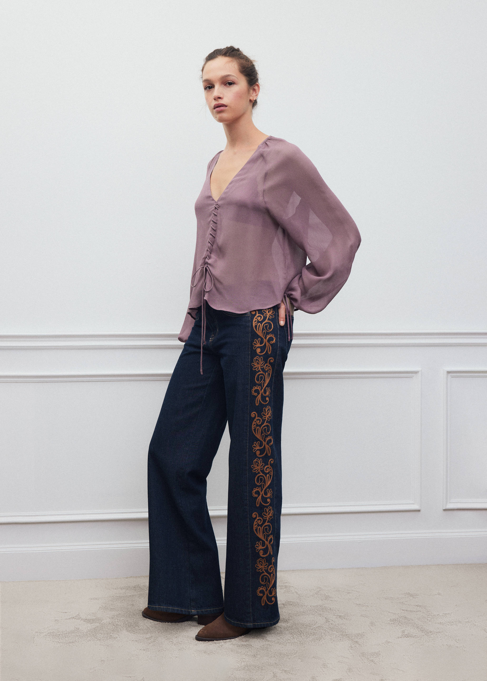 Pantalones vaqueros de color azul oscuro con silueta de pernera ancha y bordado floral naranja en el lateral.