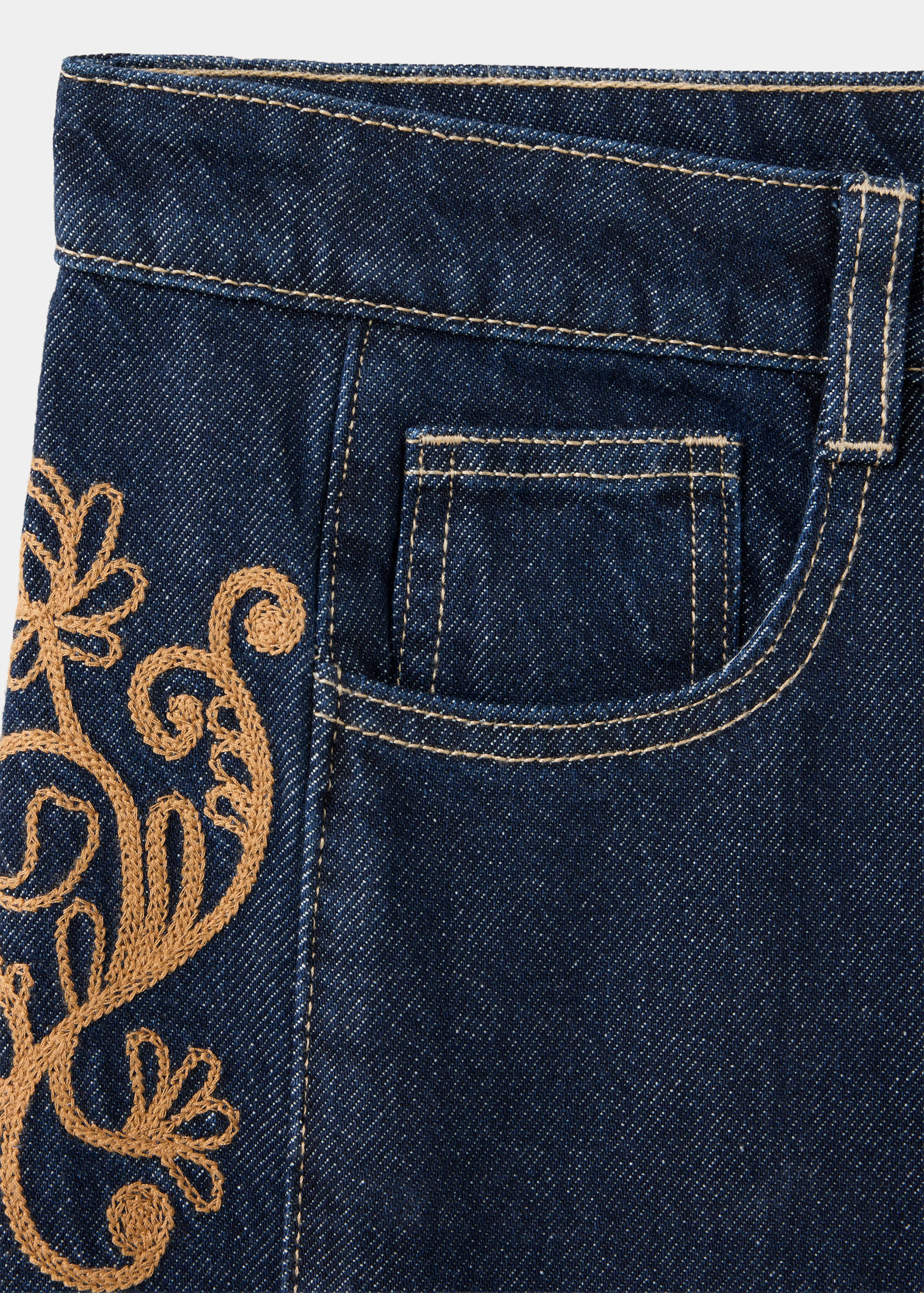Primer plano de unos pantalones vaqueros de color azul oscuro con bordados tostados y costuras en contraste.