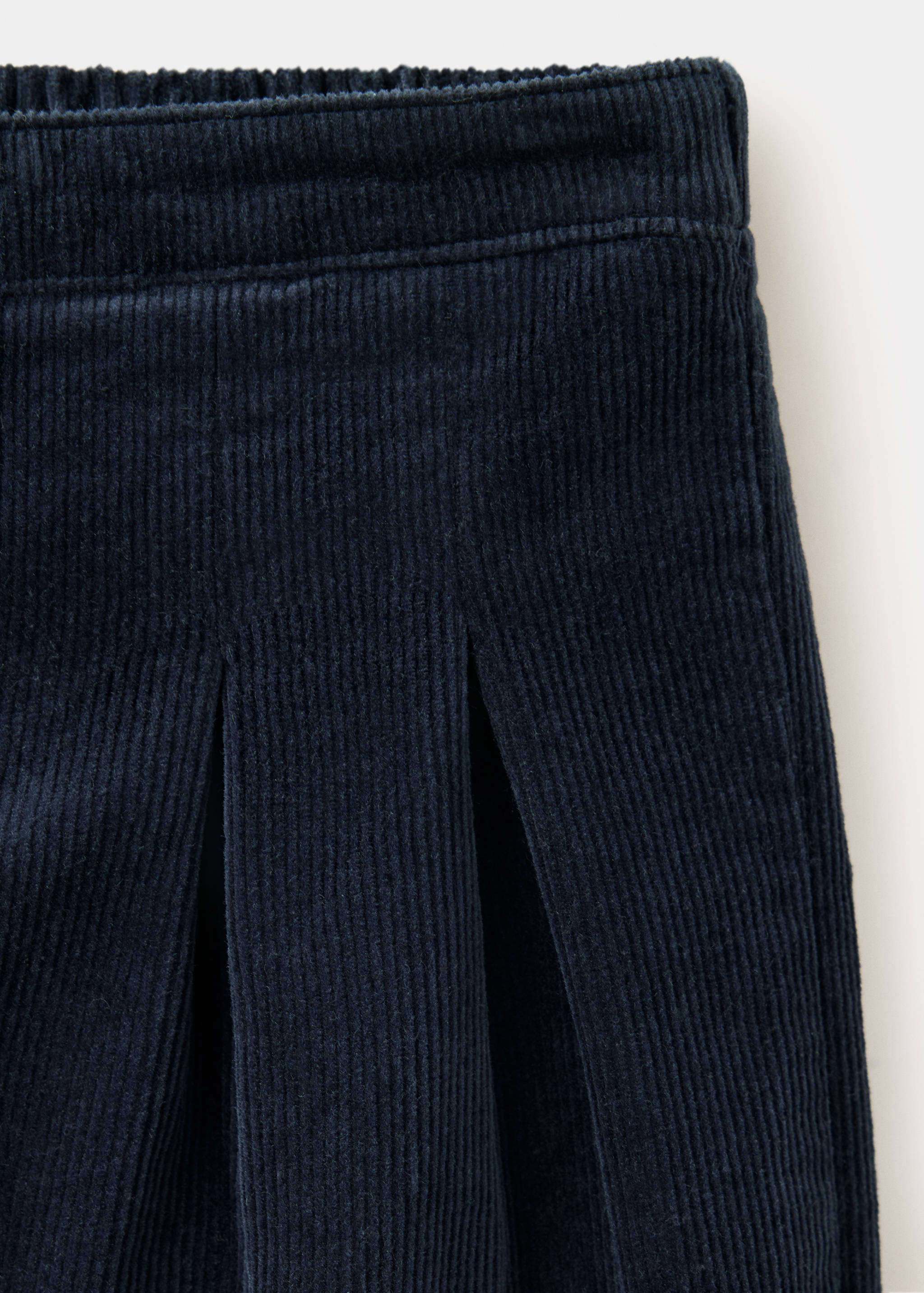 Detalle de pantalones de pana azul marino que muestra la cintura y los pliegues.