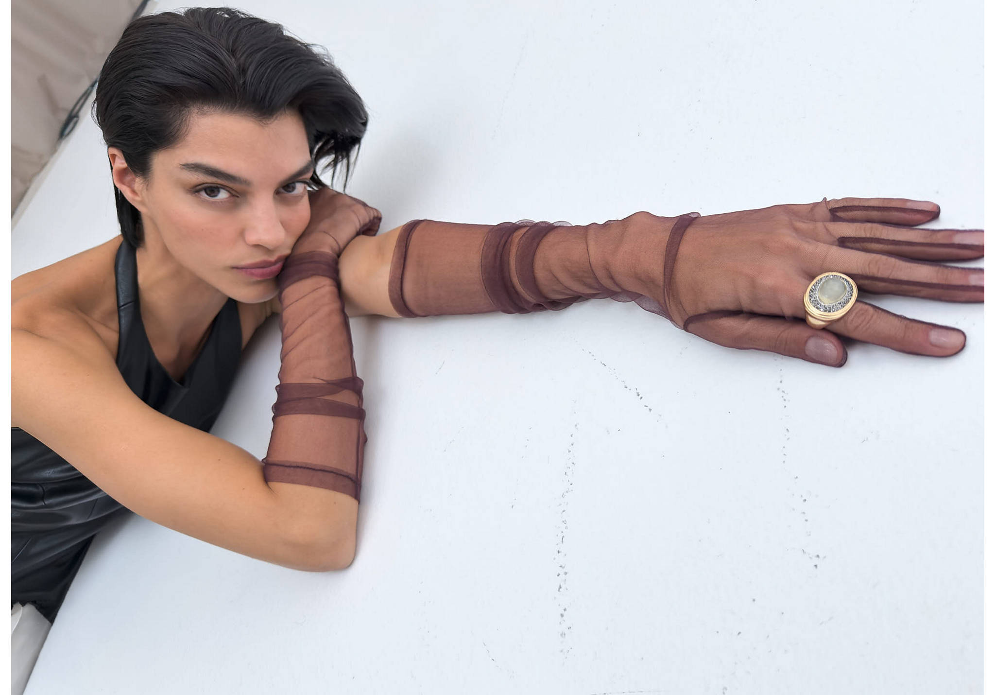 Brown sheer tulle gloves extending past the elbows, worn with a statement ring.