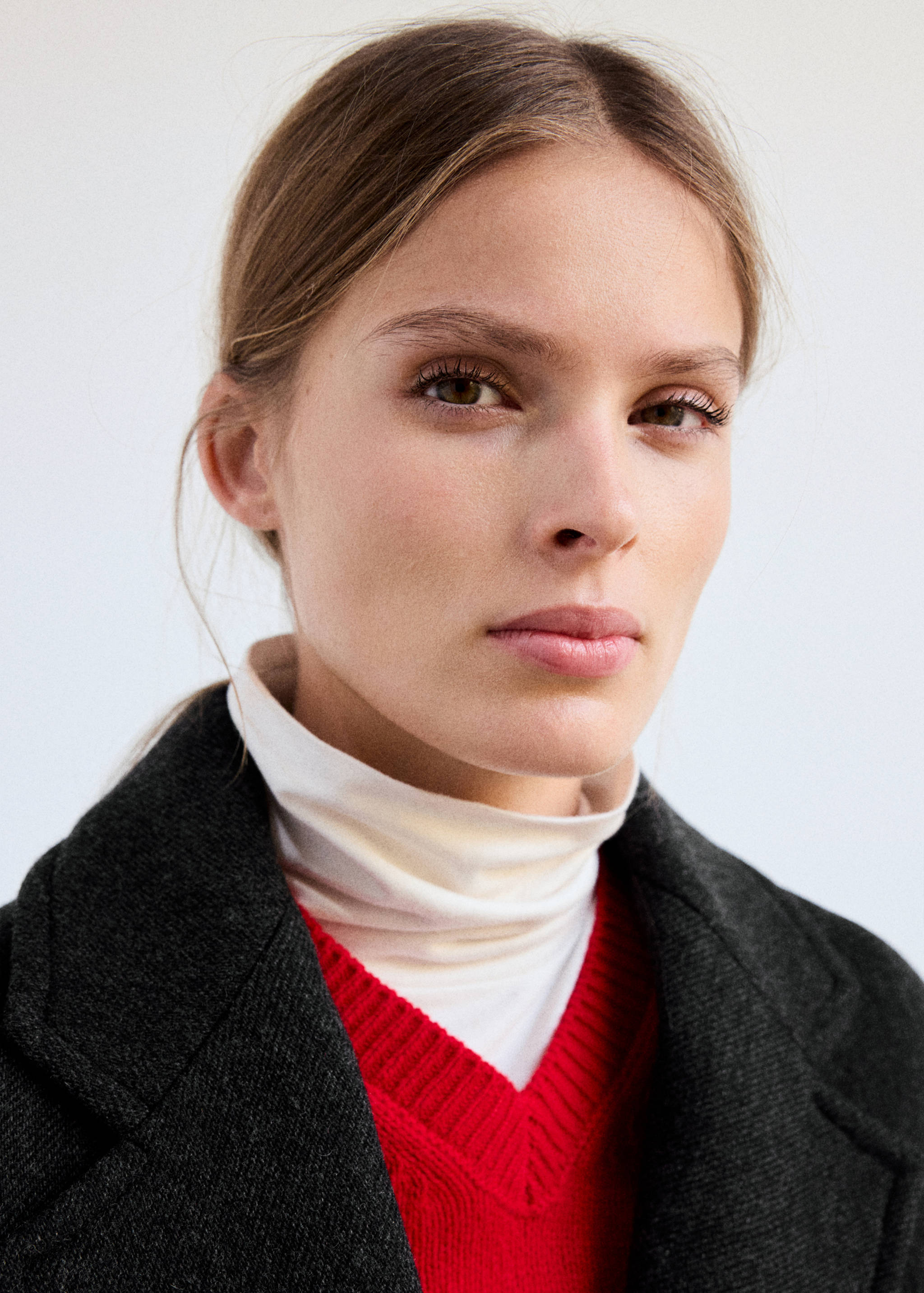 Dark grey coat worn over a red v-neck jumper and white top, shown in a close-up.