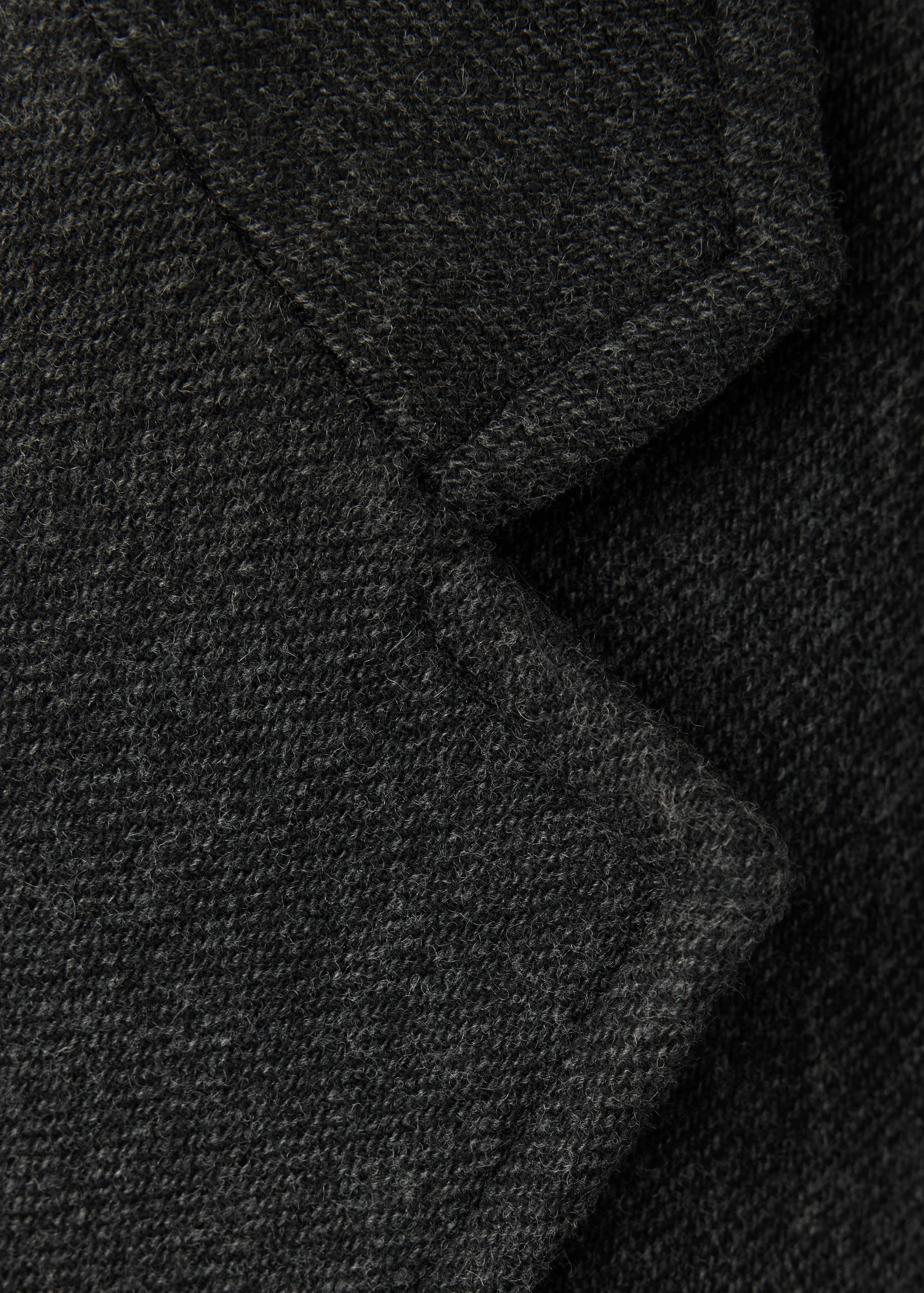 Close-up of the dark grey textured coat fabric and lapel.