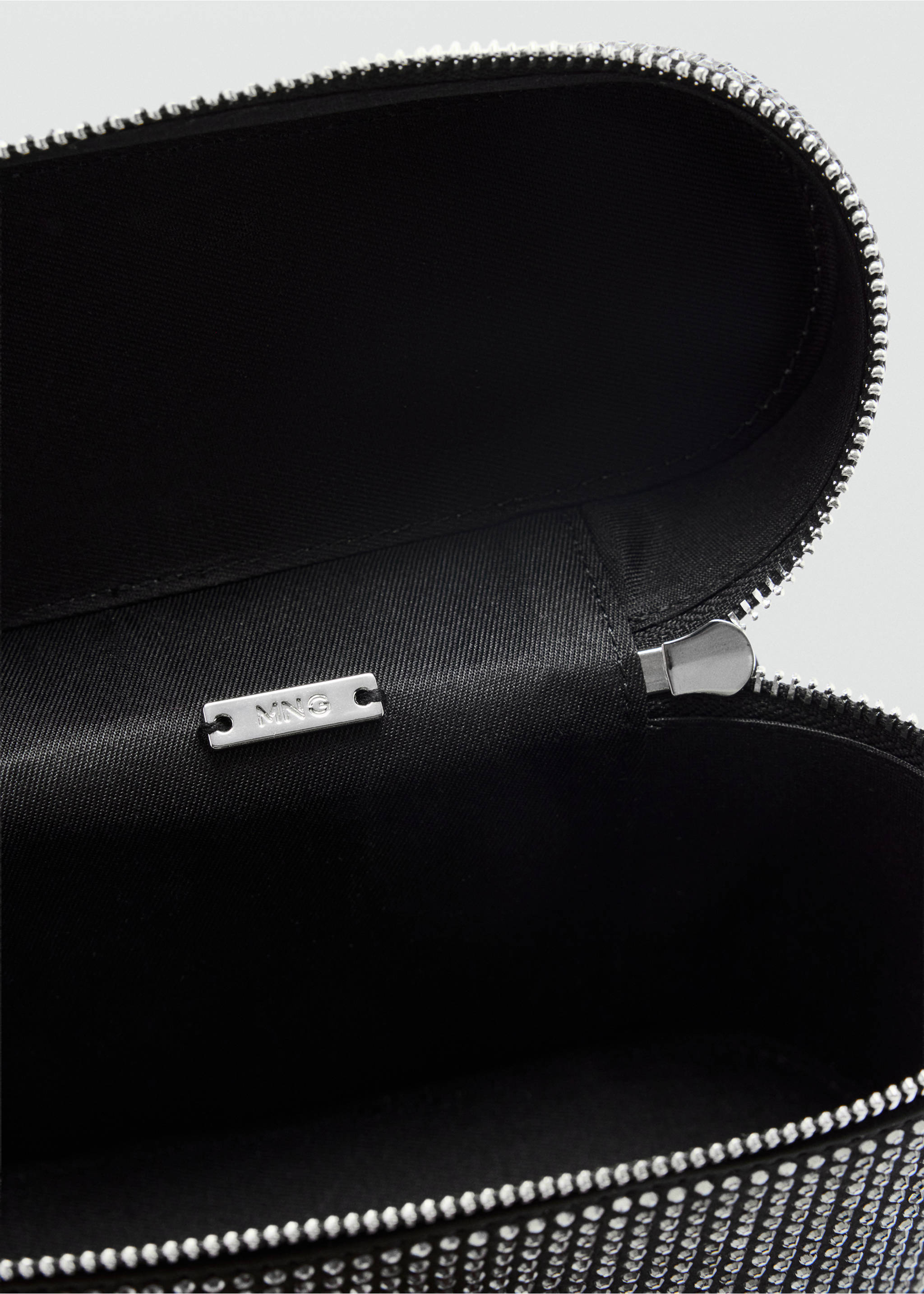 Close-up interior of a black rhinestone-embellished handbag showing the lining and branded metal plaque., Black. Ref: 37049114-00.