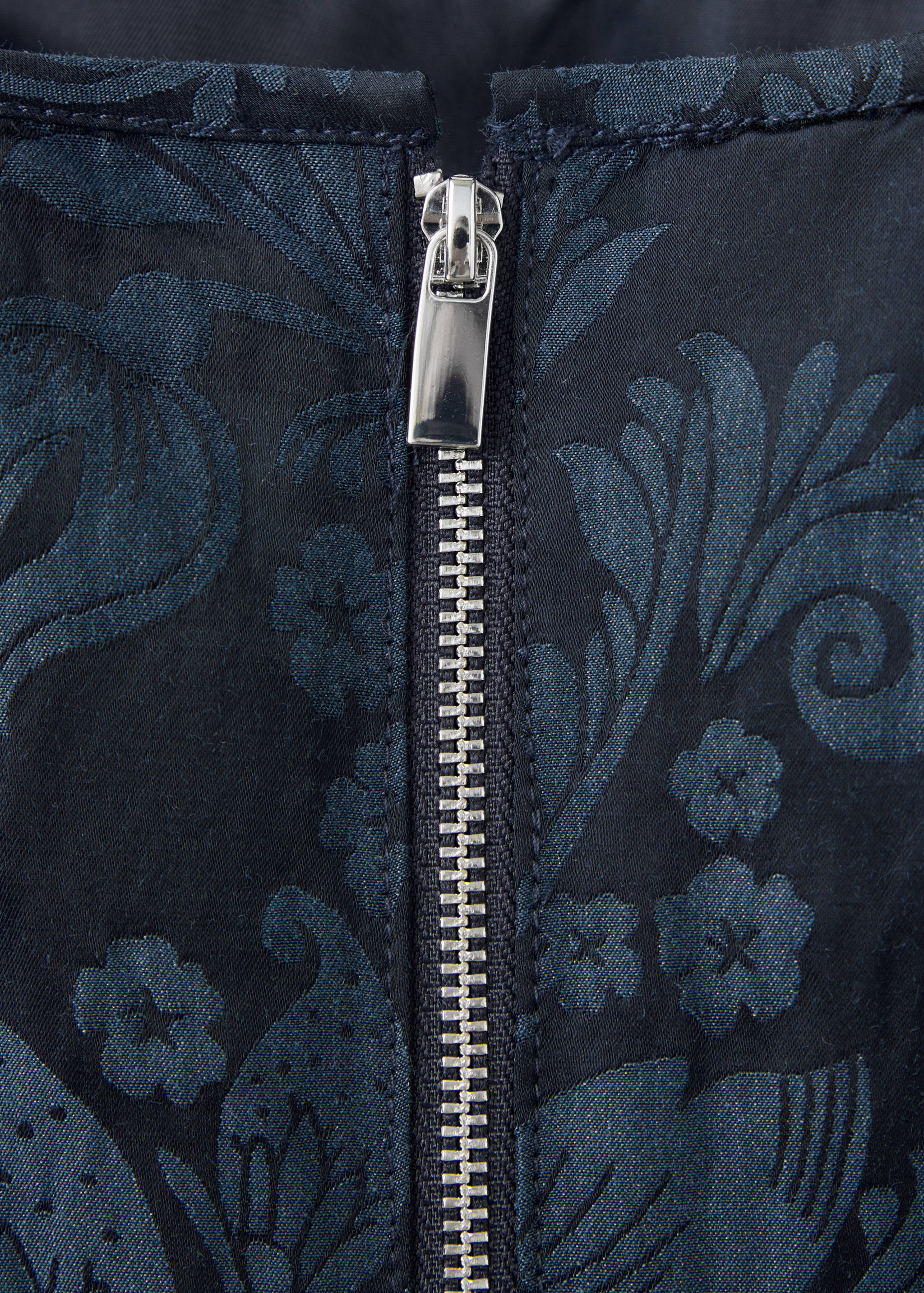 Close-up of a navy blue top with a tonal jacquard floral pattern and a silver zip.
