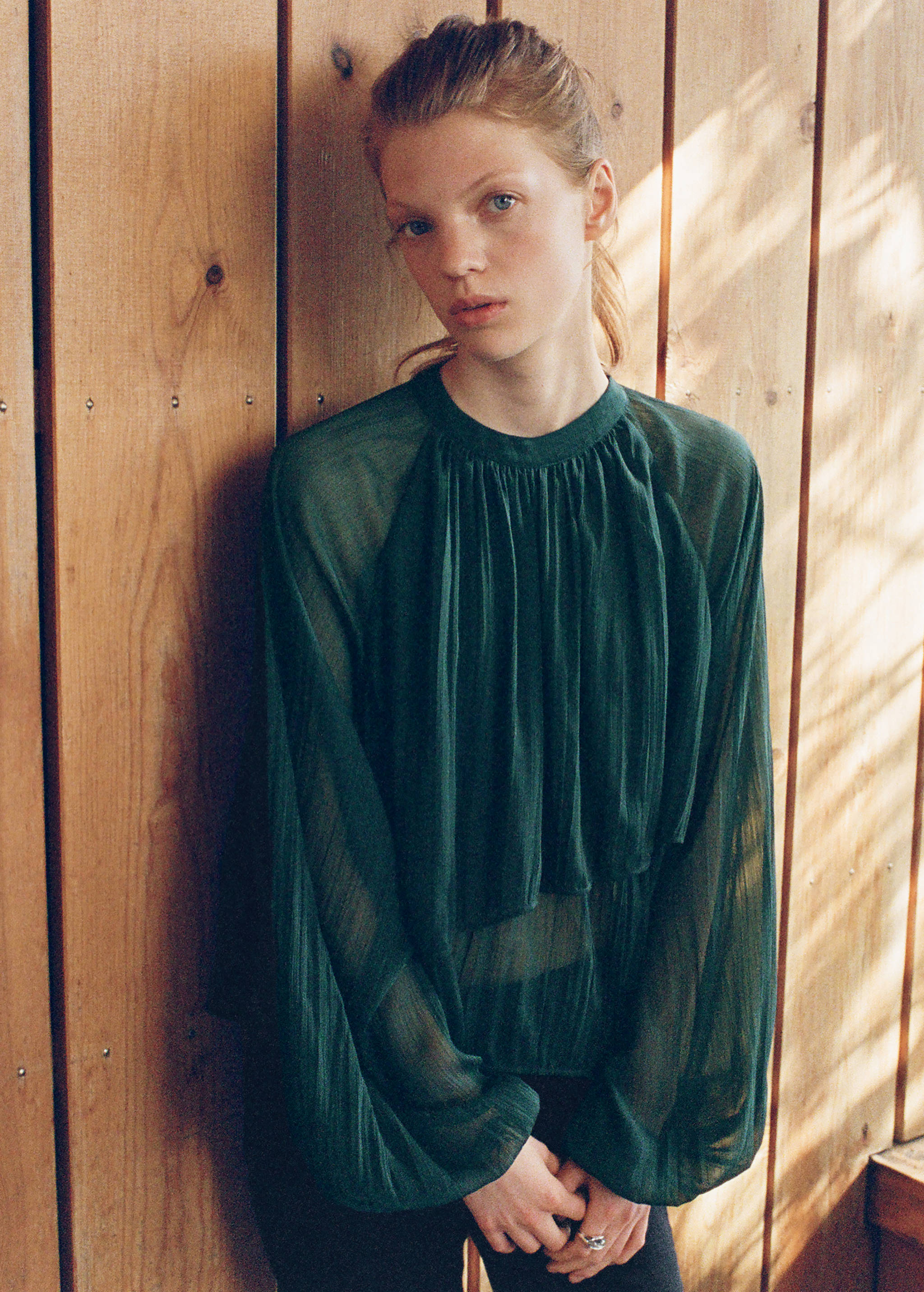 Dark green sheer long-sleeve blouse with a round neck and pleated front.