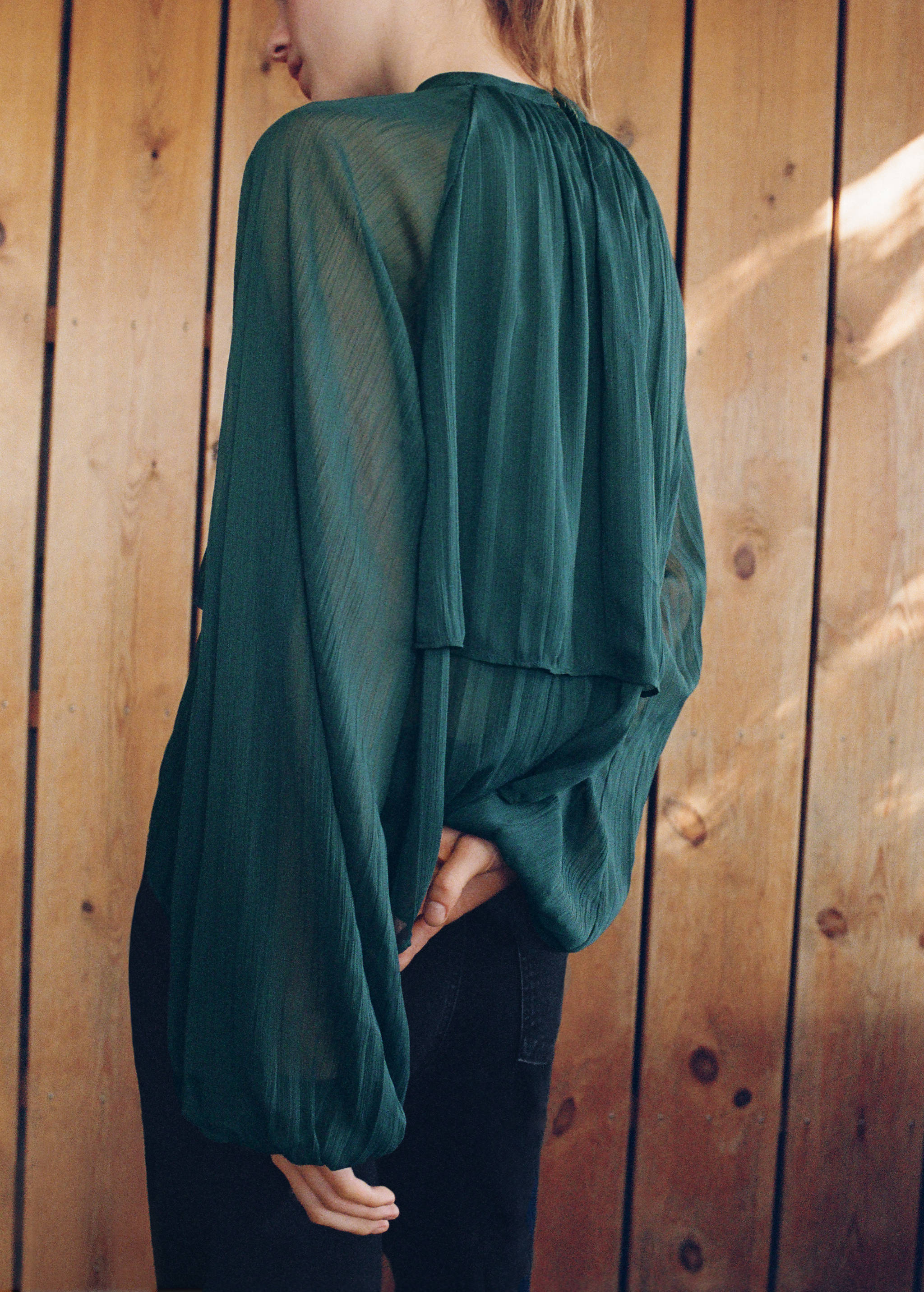 Dark green long-sleeve blouse with a high neck and back capelet, shown from behind.