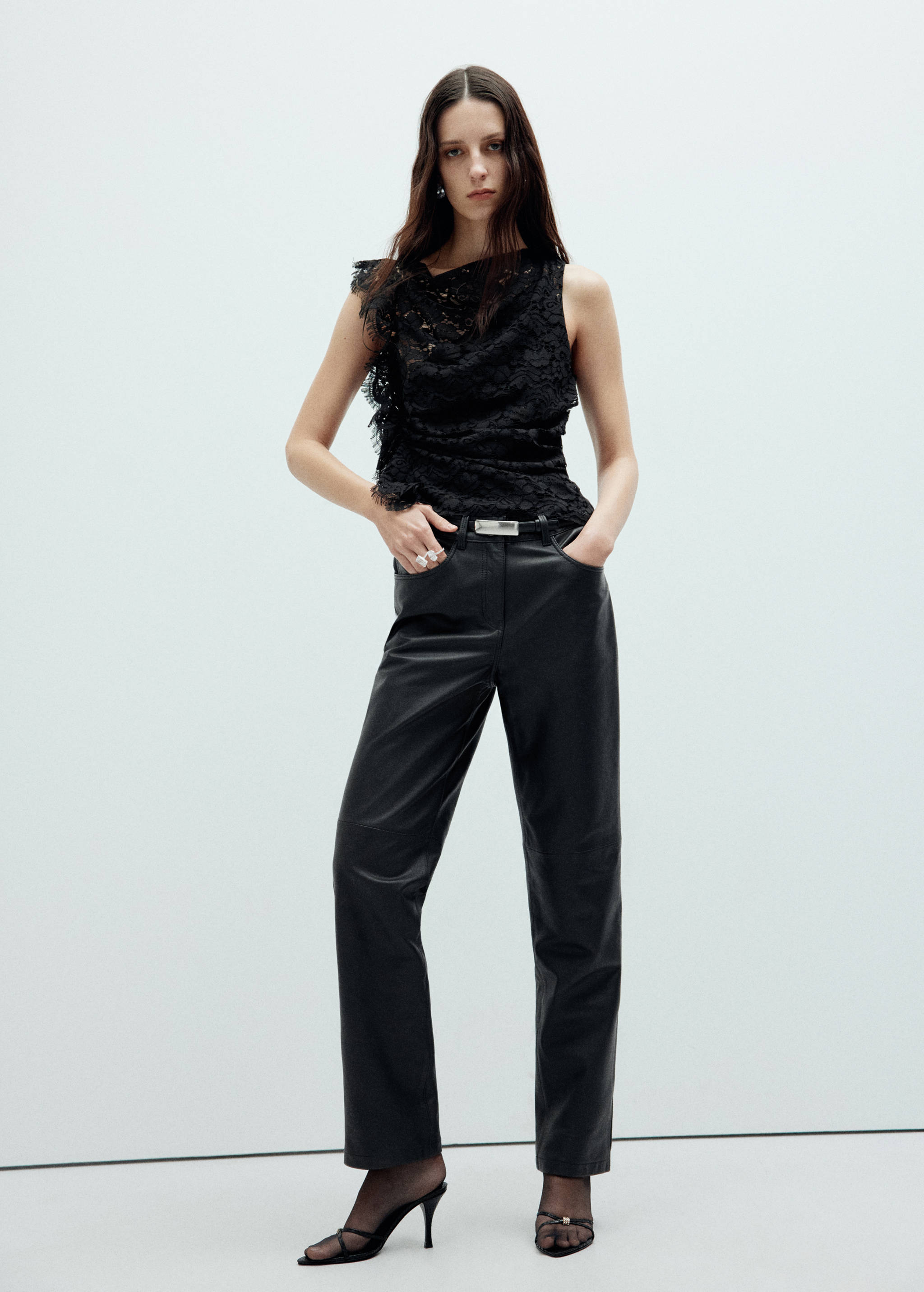 Black lace sleeveless top with asymmetric ruffle trim, worn with black trousers.