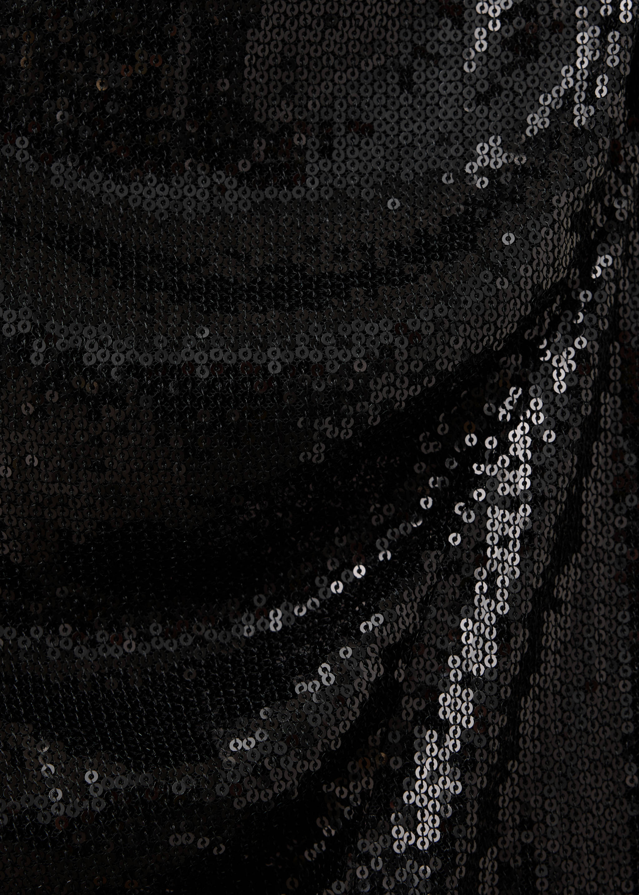 Close-up of black sequinned dress fabric showing the textured, reflective finish.