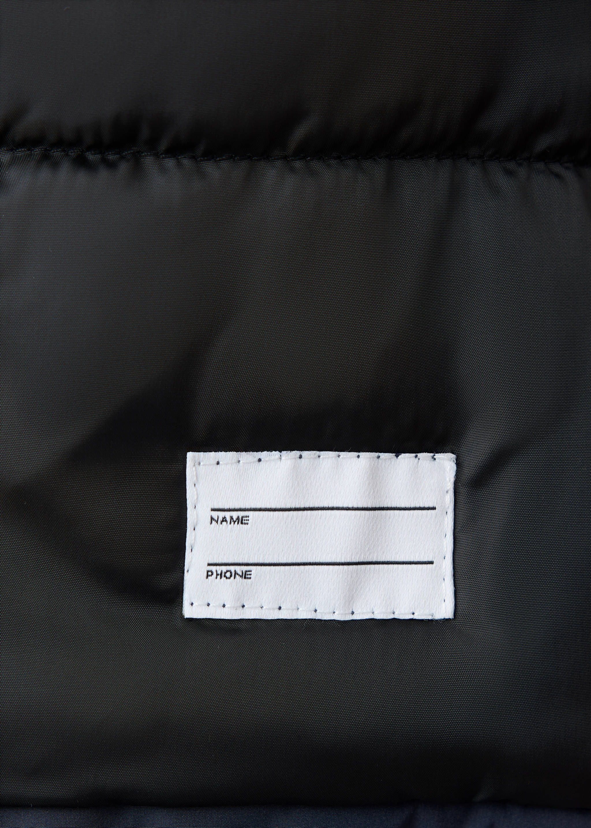 Close-up of the black anorak fabric showing an interior name and phone label.