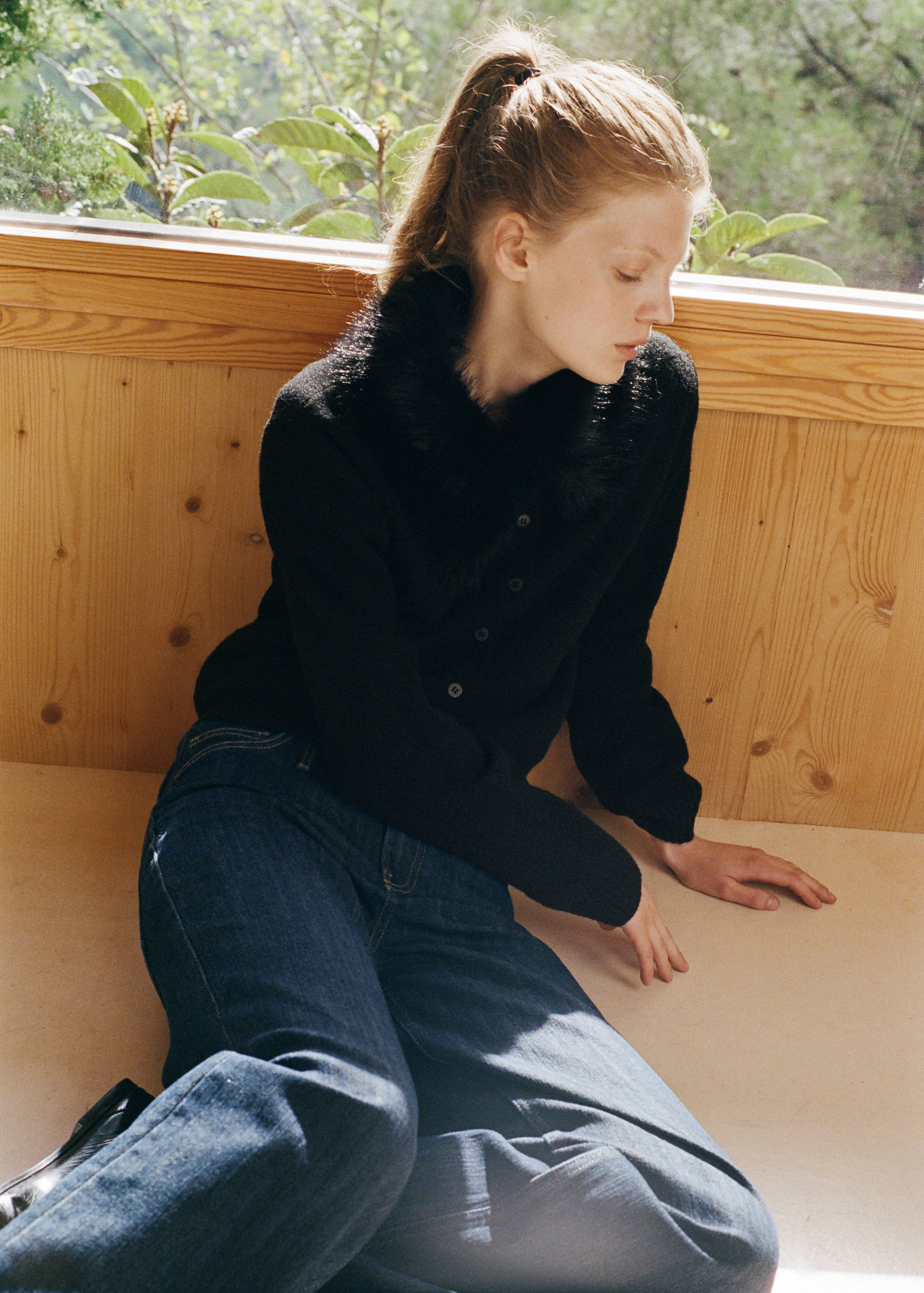 Black cardigan with faux-fur collar and front buttons worn with blue denim trousers.