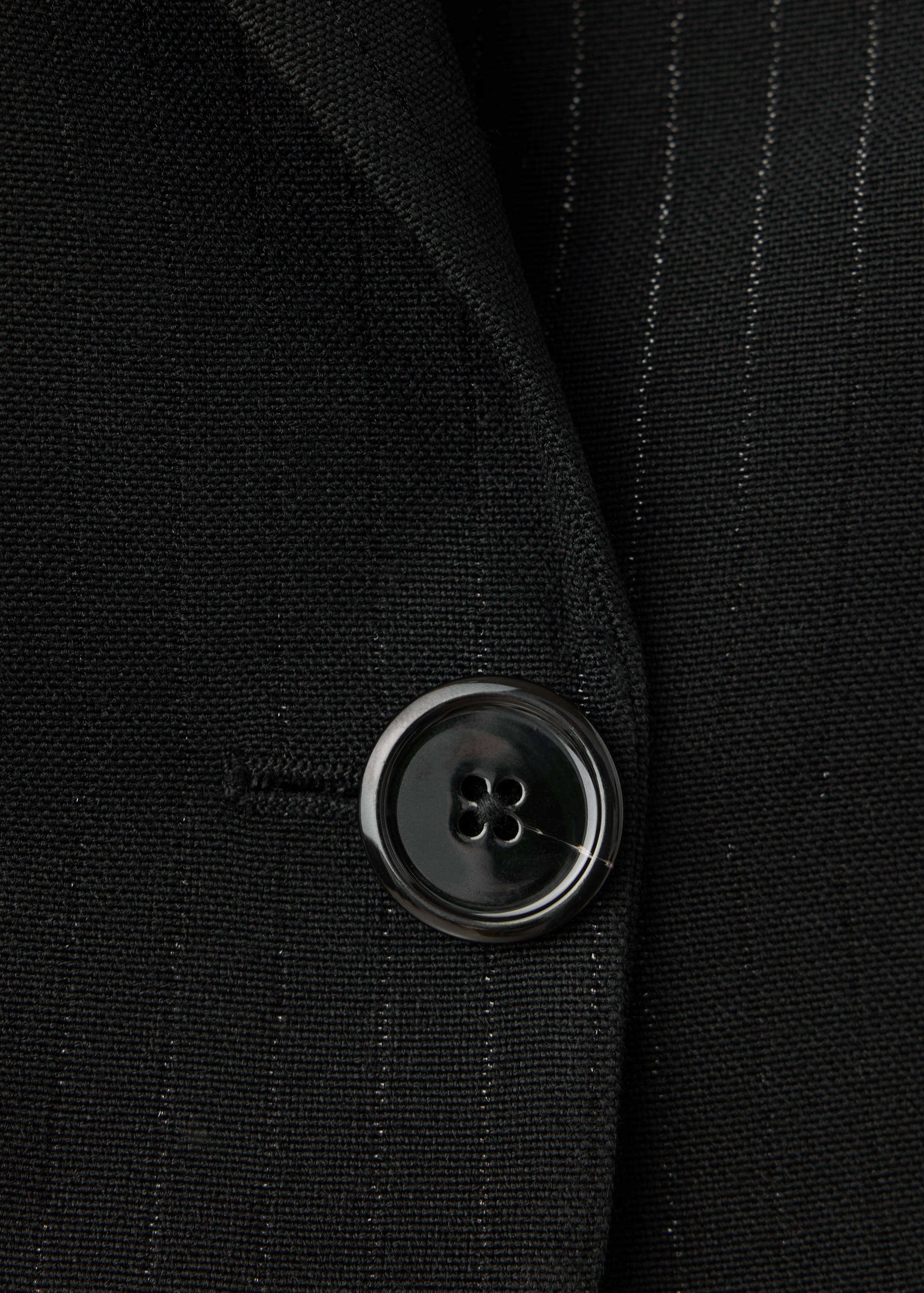 Close-up of a black pinstripe blazer showing the button detail.