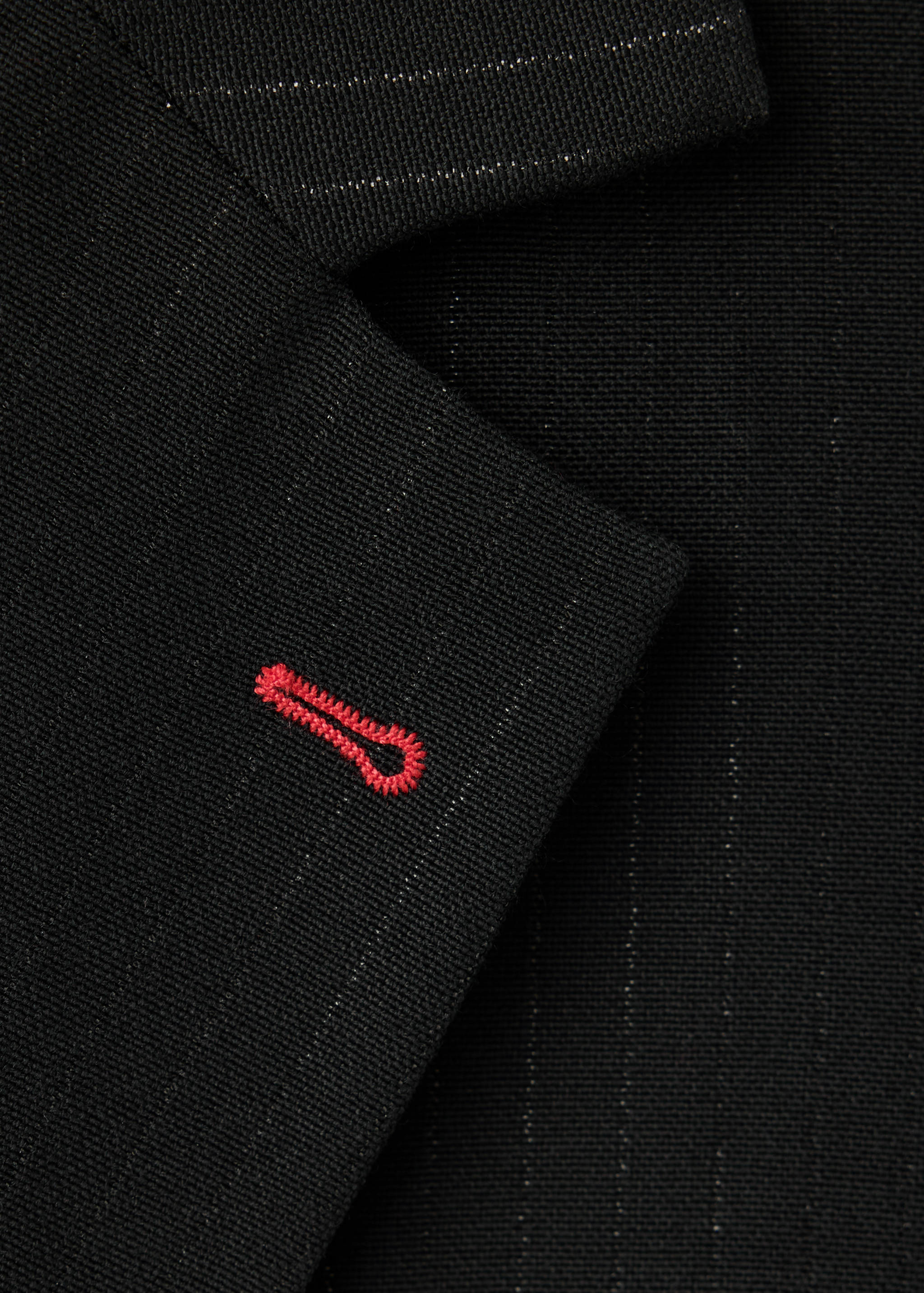 Black pinstripe blazer fabric detail with a red embroidered buttonhole.