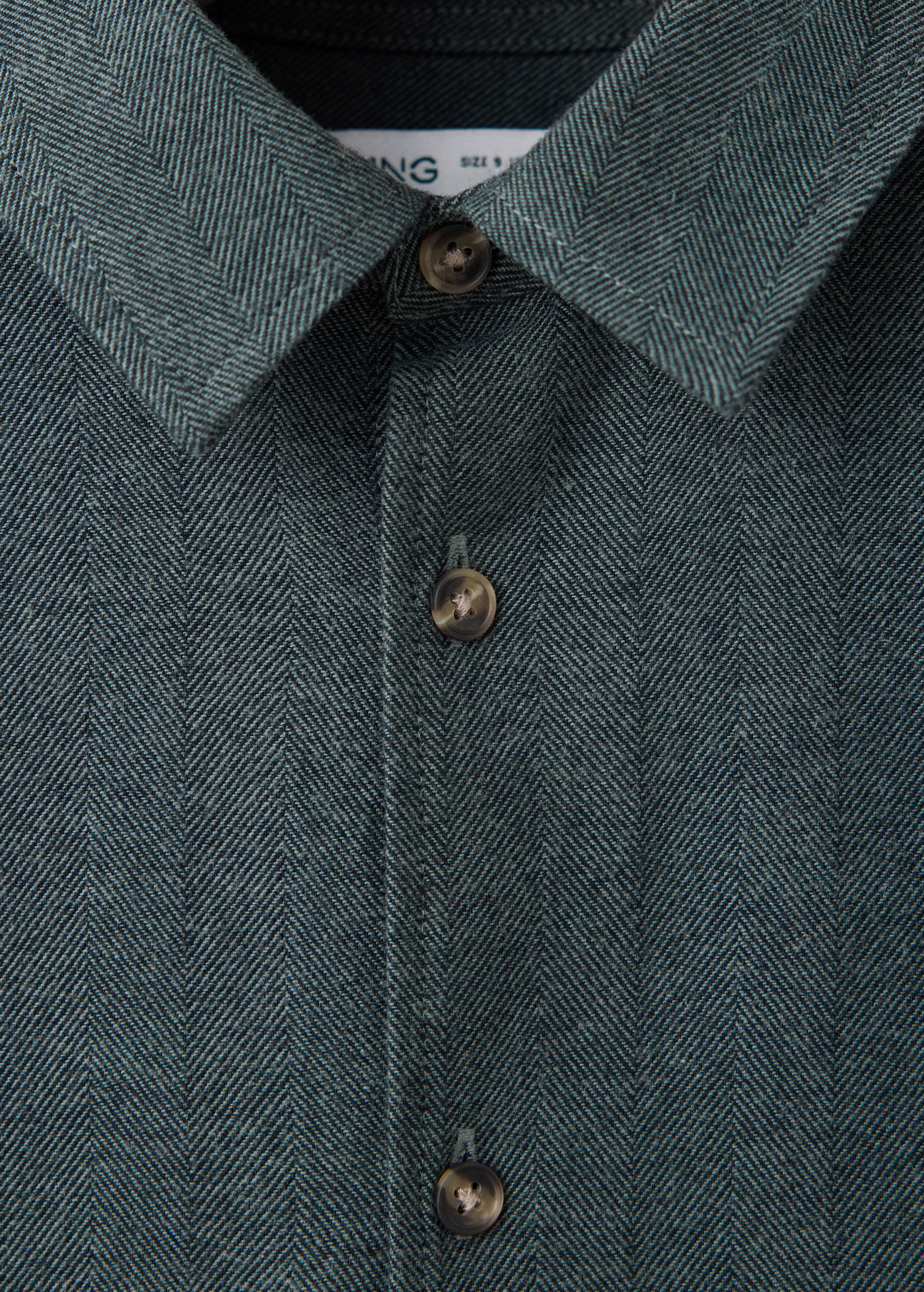 Detalle del cuello y la tapeta de botones de una camisa espiga de color verde oscuro.
