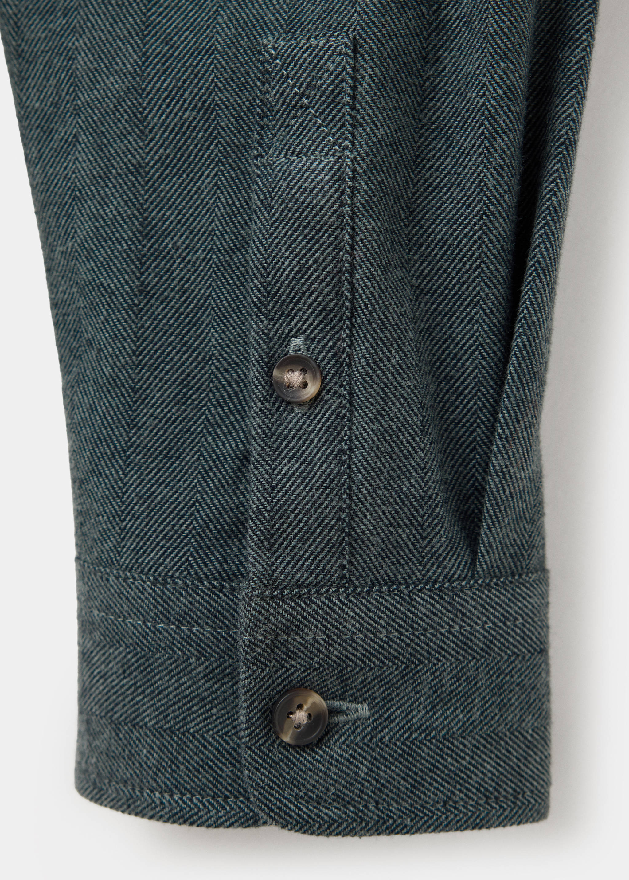 Primer plano del puño de una camisa verde oscura de espiga con abotonadura.