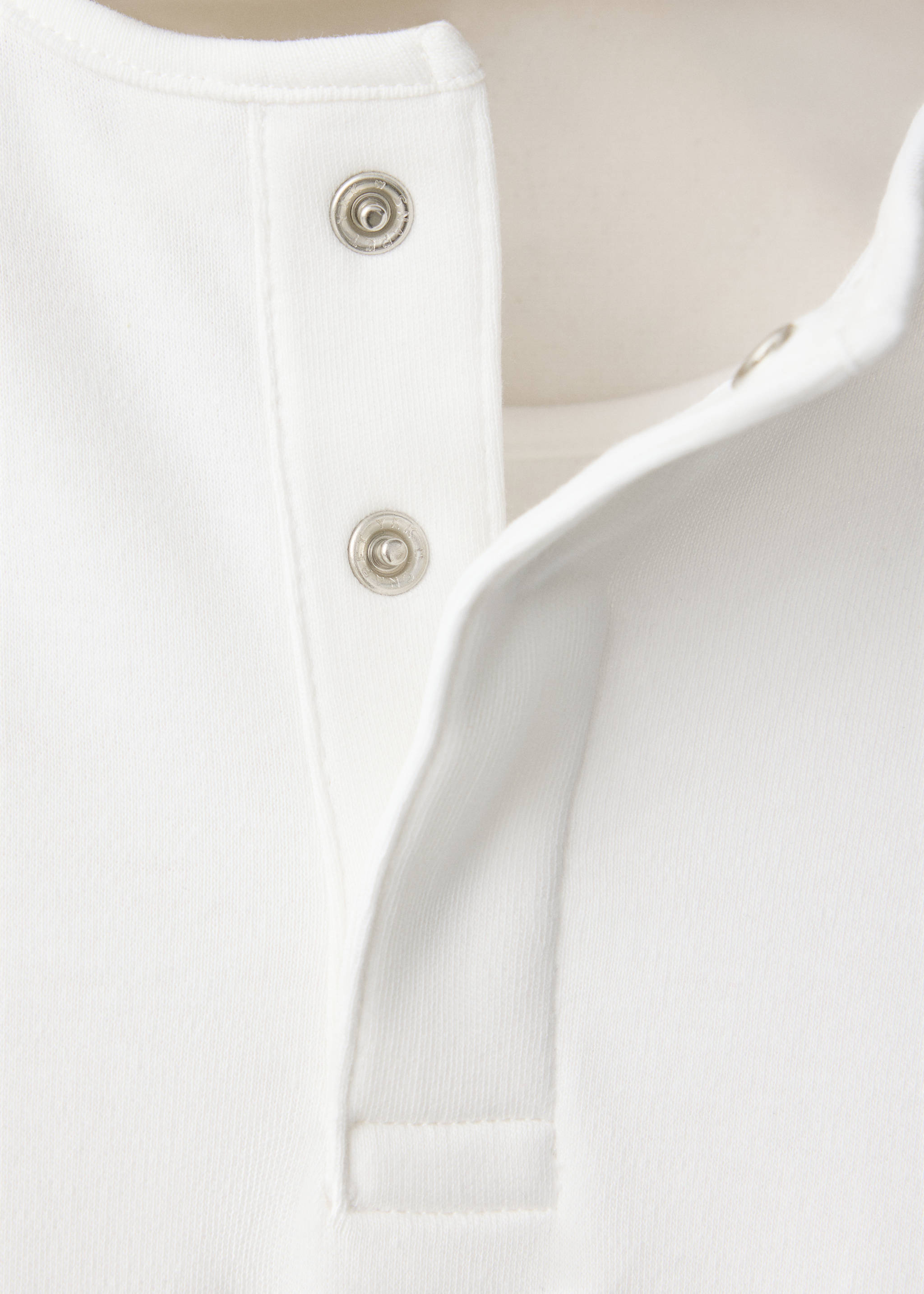 Close-up of a white pyjama neckline with silver-toned snap fasteners.