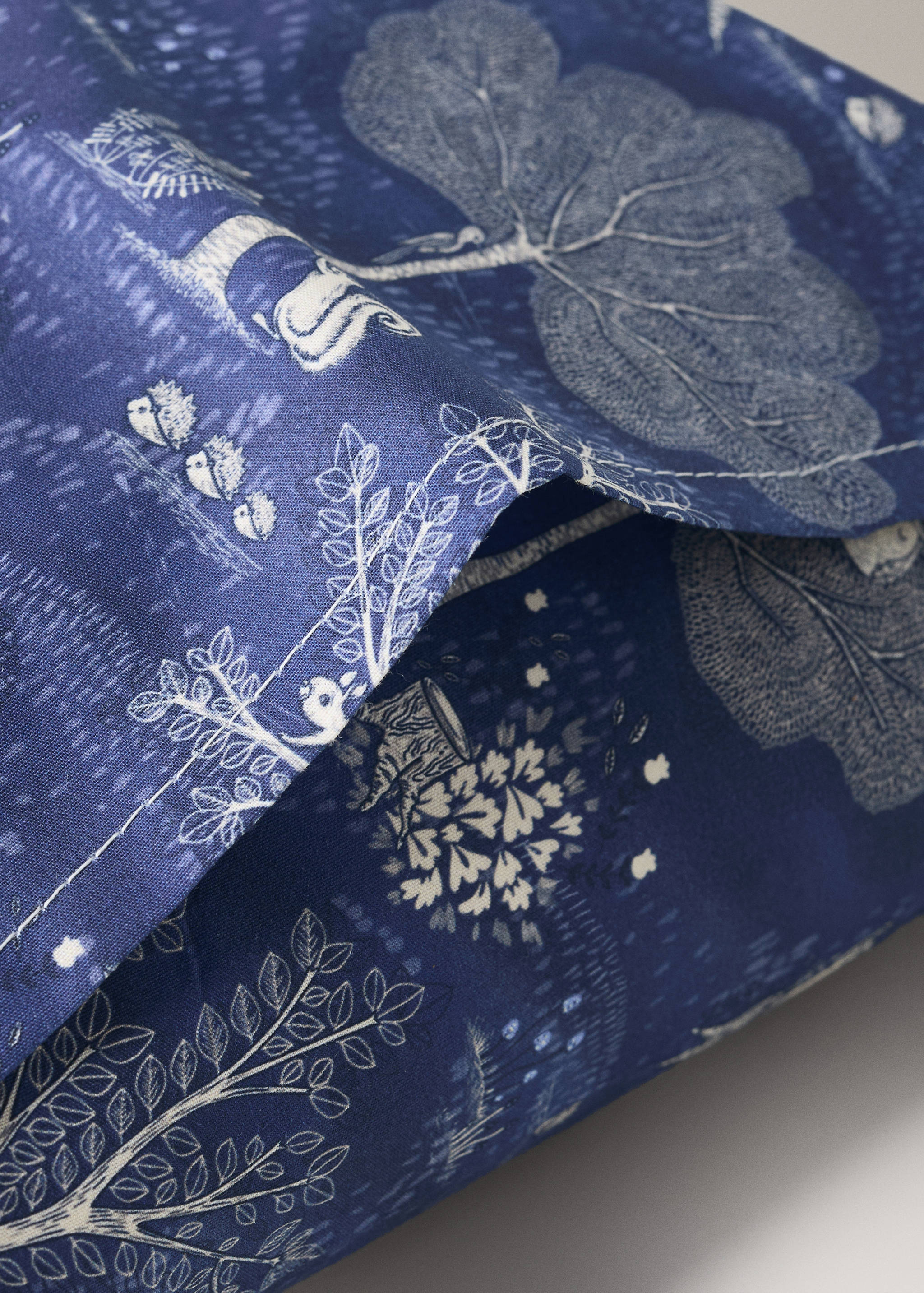 Blue printed cot pillowcase with a white botanical woodland design.