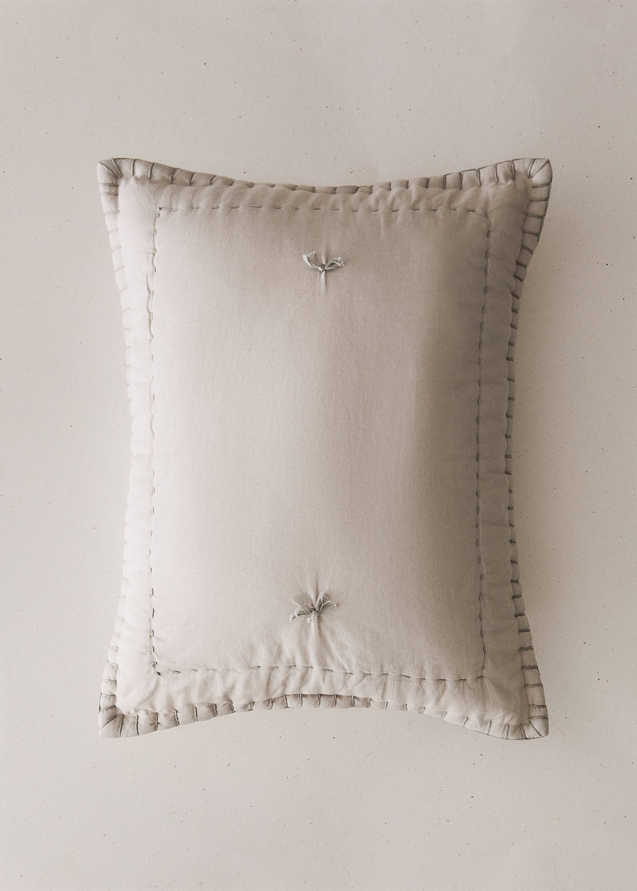 Light beige bed cushion cover with contrast stitching and tufted knot details.
