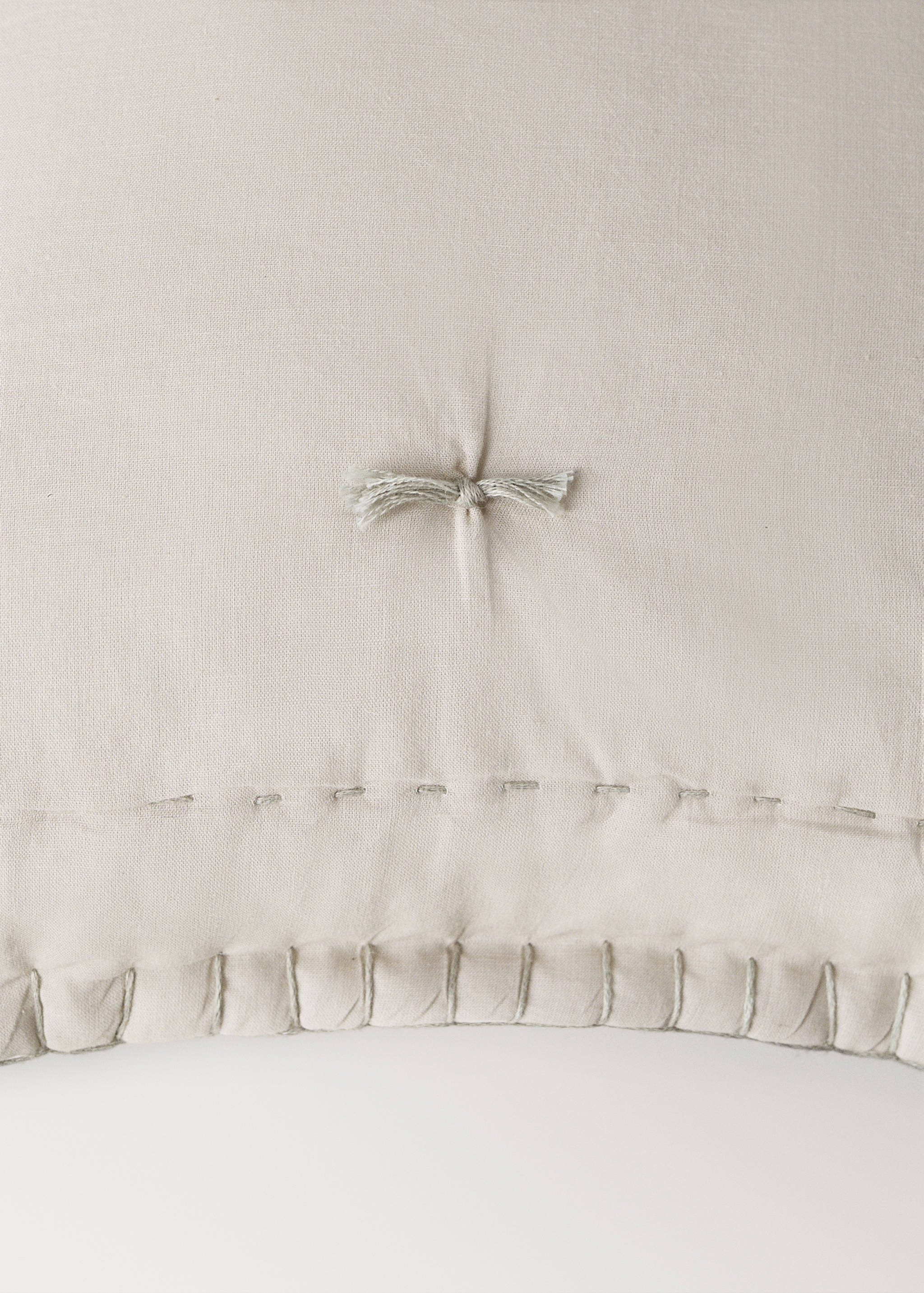 Beige cushion cover detail with tufting and decorative stitching.
