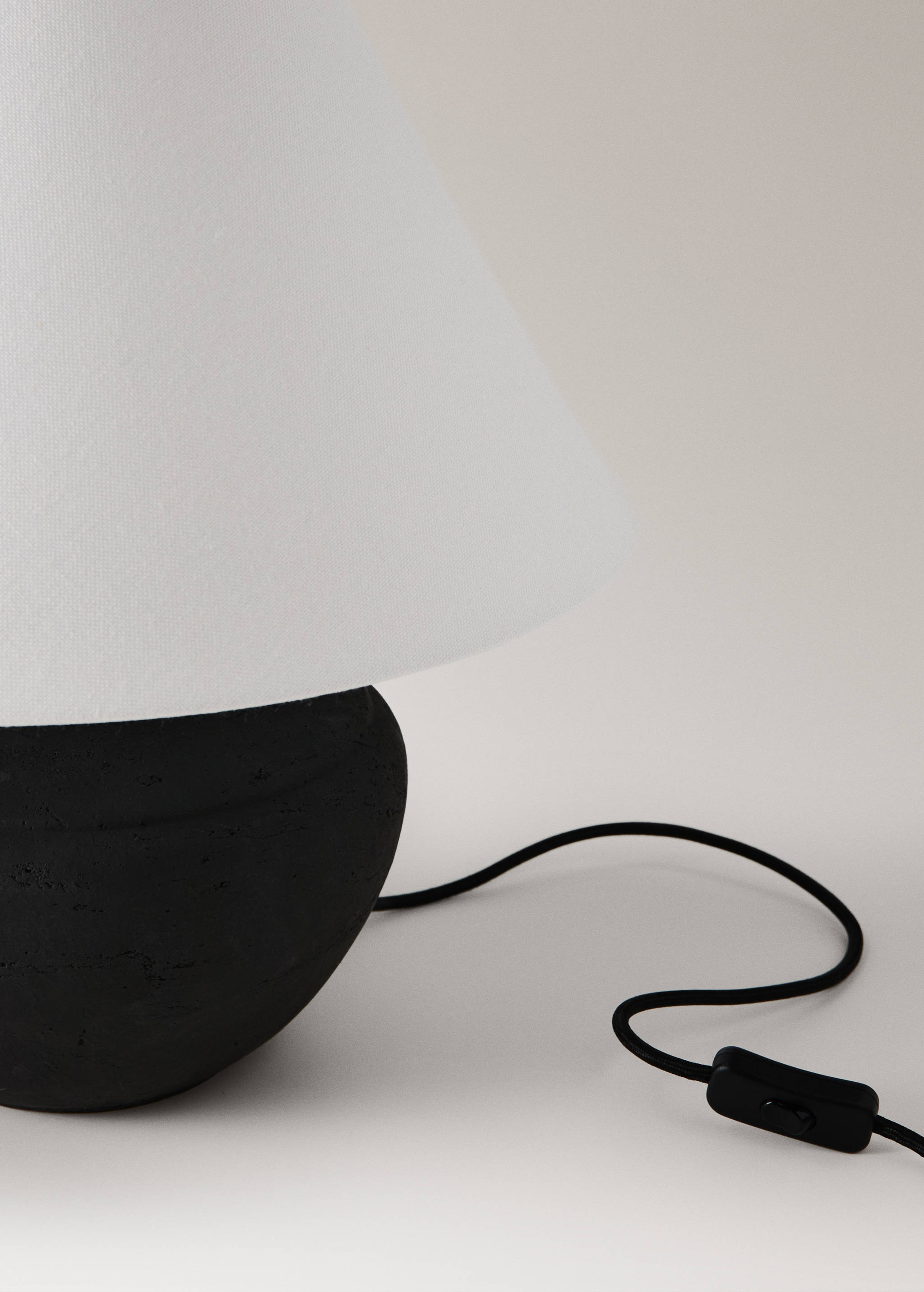 Close-up of a table lamp with a black textured base and white fabric shade.