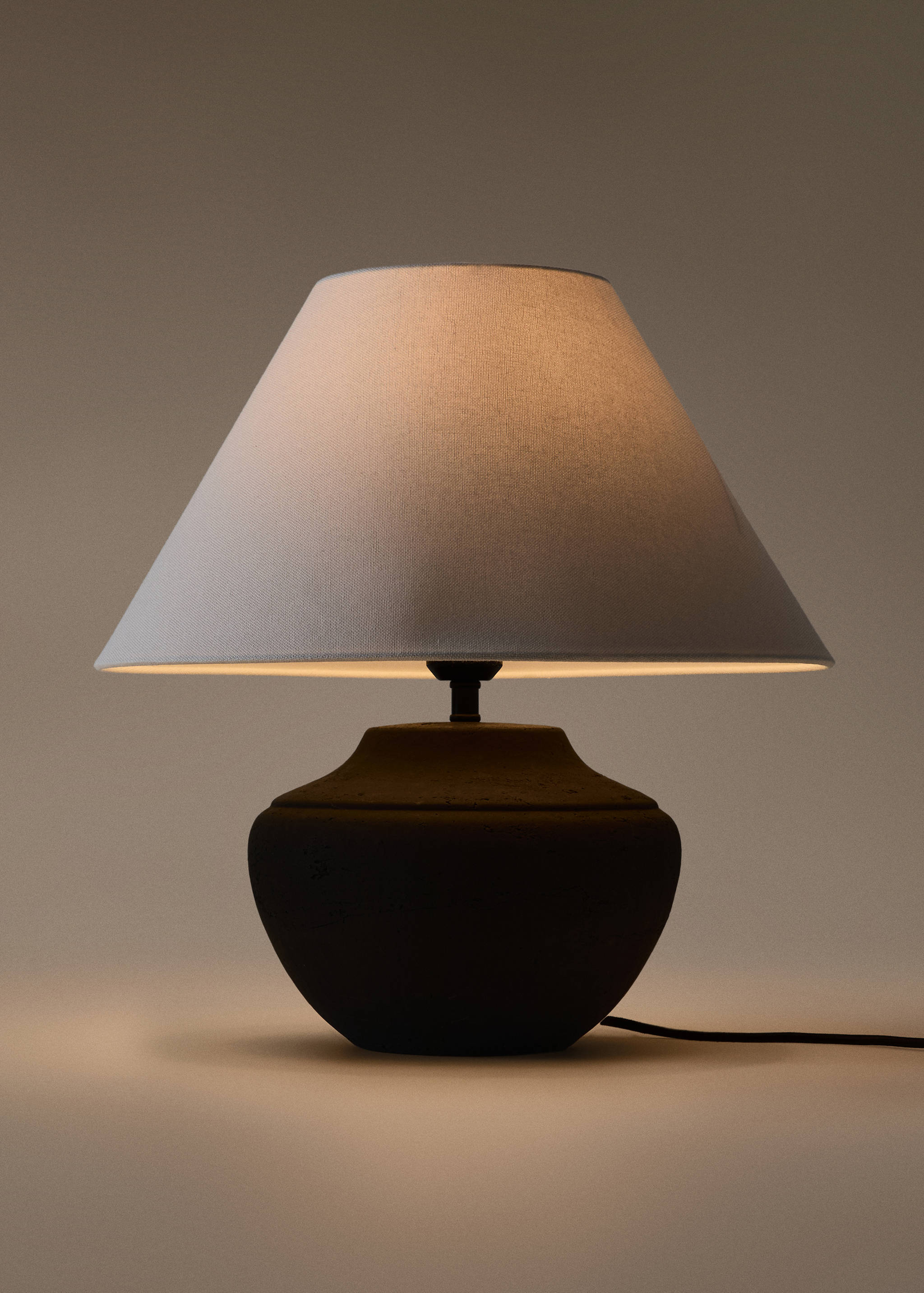 Lit table lamp with a dark rounded base and a light fabric lampshade.