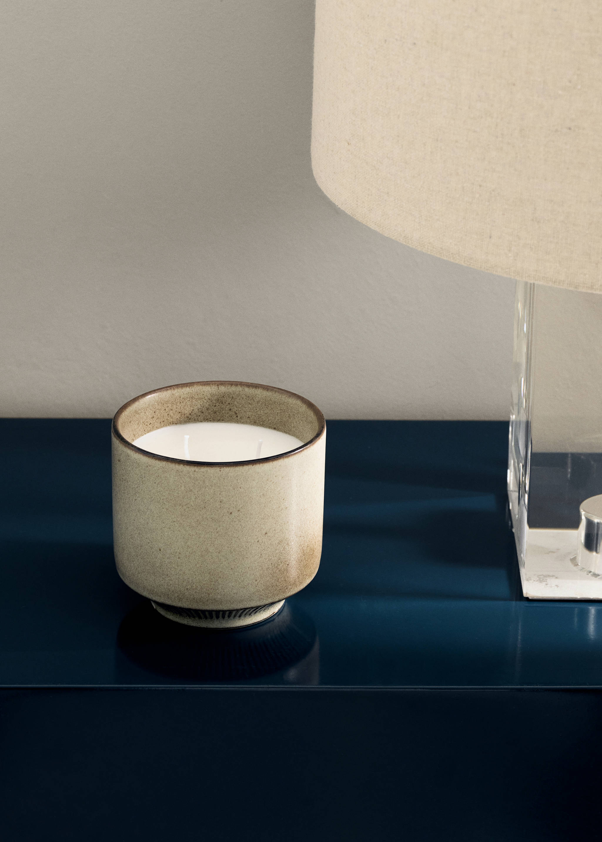 Speckled beige and brown ceramic candle on a dark blue surface.