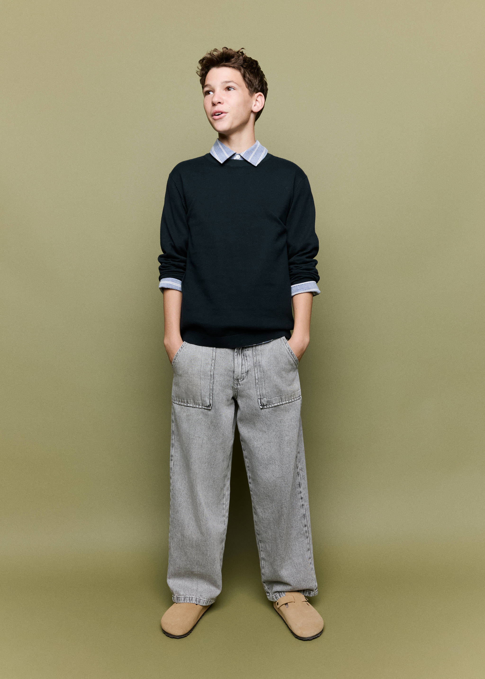 Dark green crew-neck jersey sweater worn layered over a striped shirt.