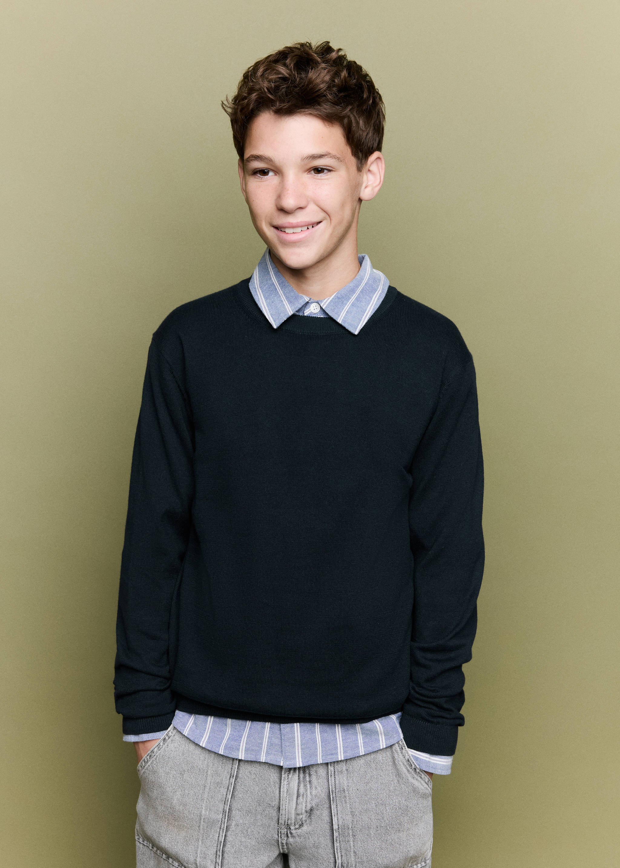 Dark blue crew neck jersey worn over a striped shirt.