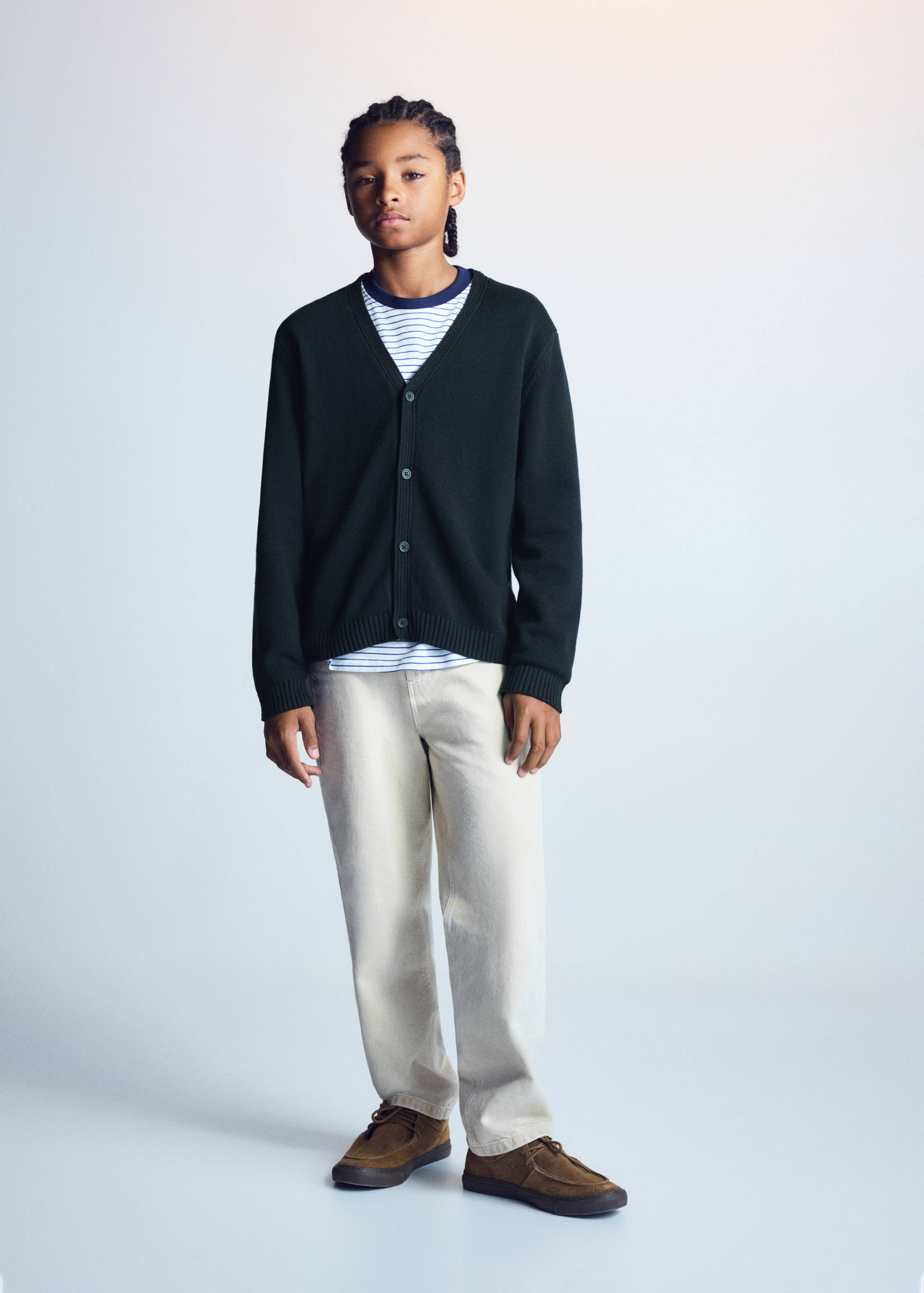 Dark green knitted V-neck cardigan worn with a striped t-shirt and light trousers.