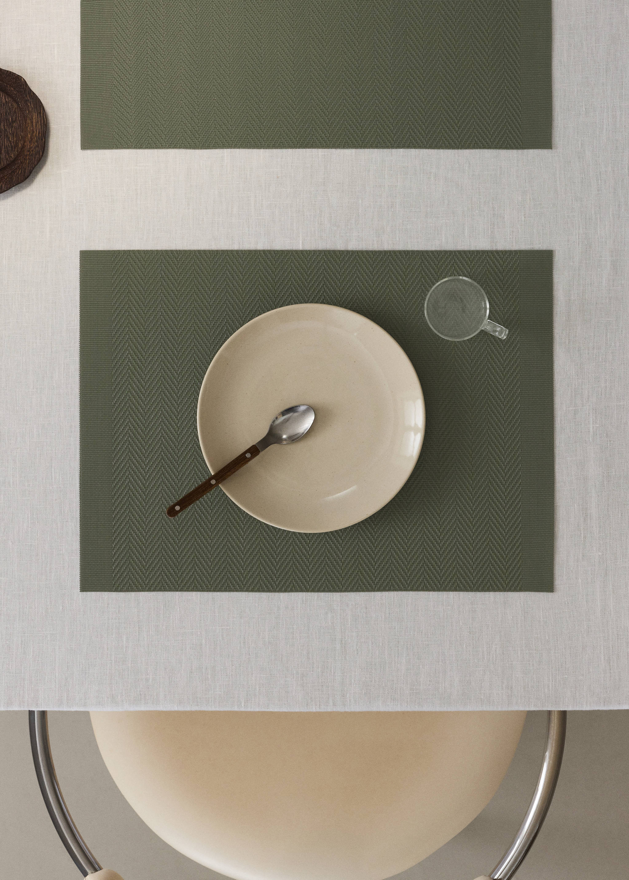 Olive green herringbone placemat on a table set with a plate and spoon.