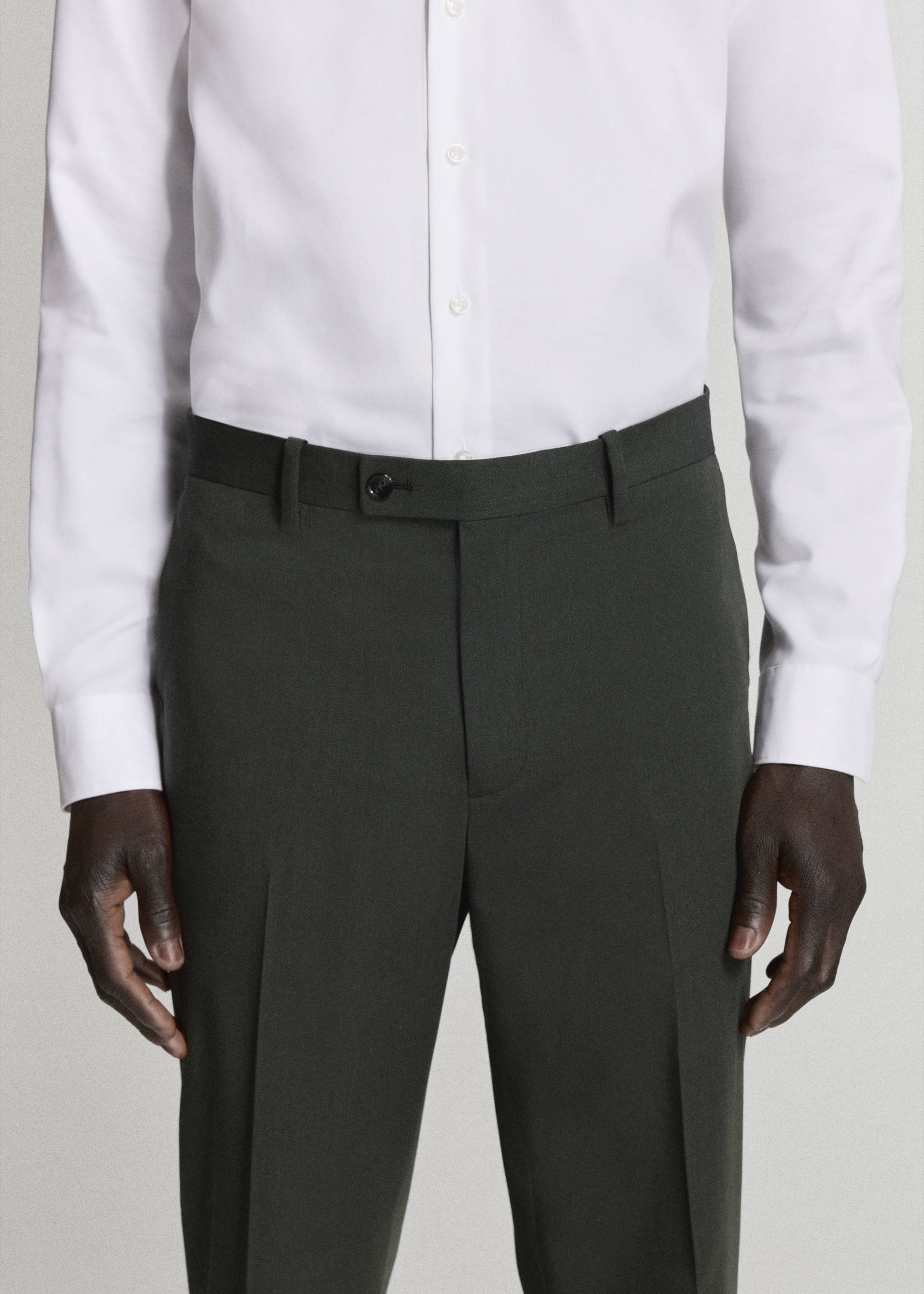Dark green tailored trousers with a waistband button and belt loops, styled with a white shirt.