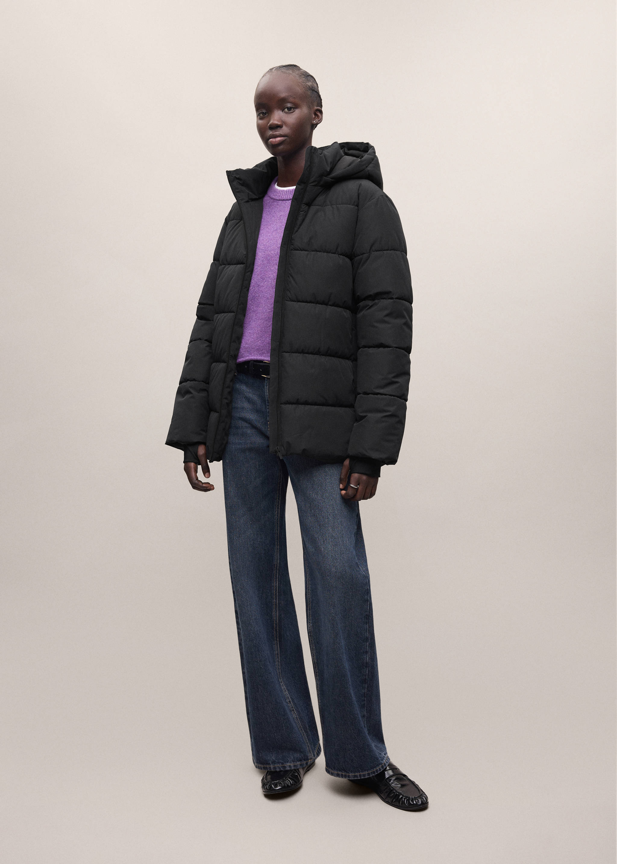 Black quilted anorak with a hood, worn with a purple sweater and blue trousers.