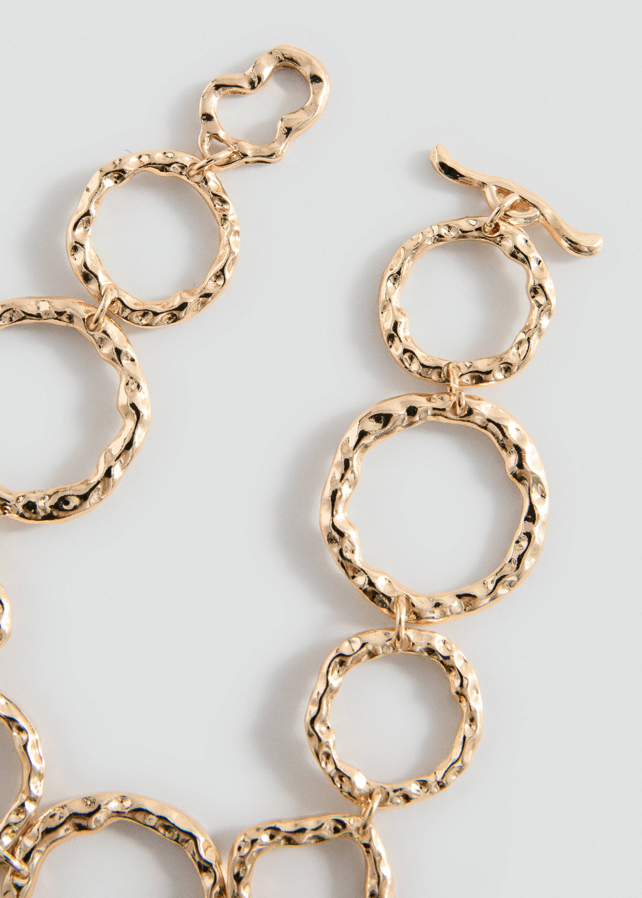 Close-up of a gold-tone hammered metal link bracelet with a T-bar clasp.