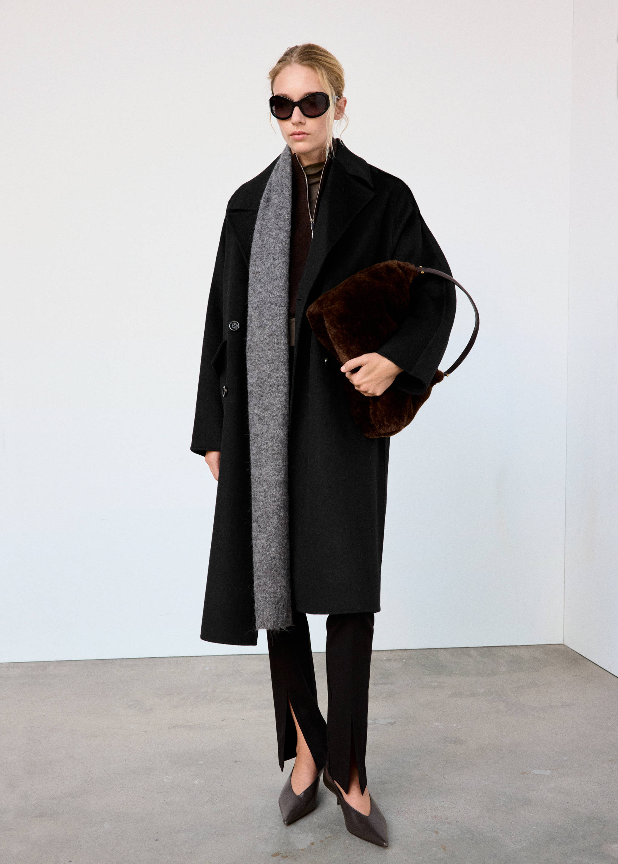 Black longline coat with lapels worn with a grey scarf and dark trousers with slits.
