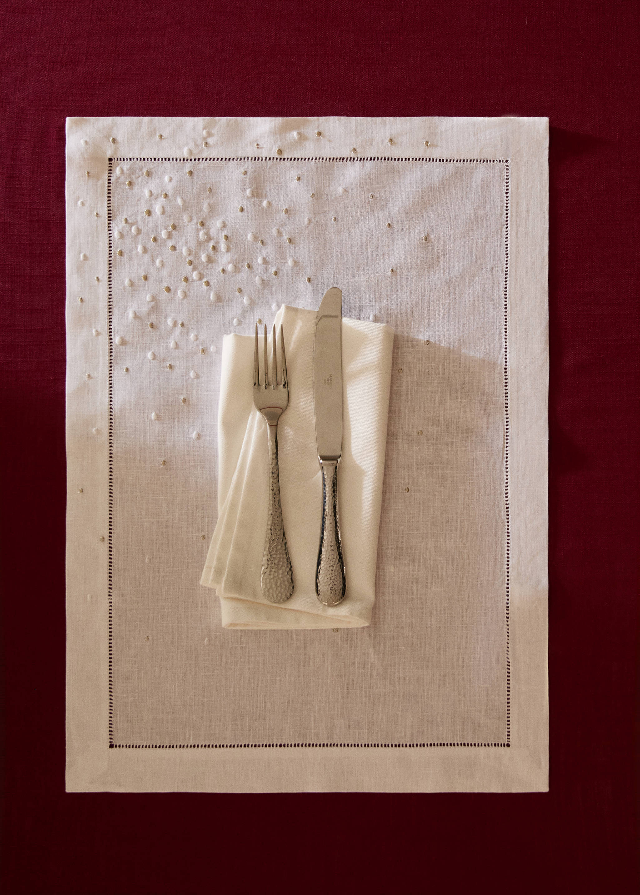 Off-white placemat with beaded embroidery and hemstitch border, styled with napkin and cutlery.