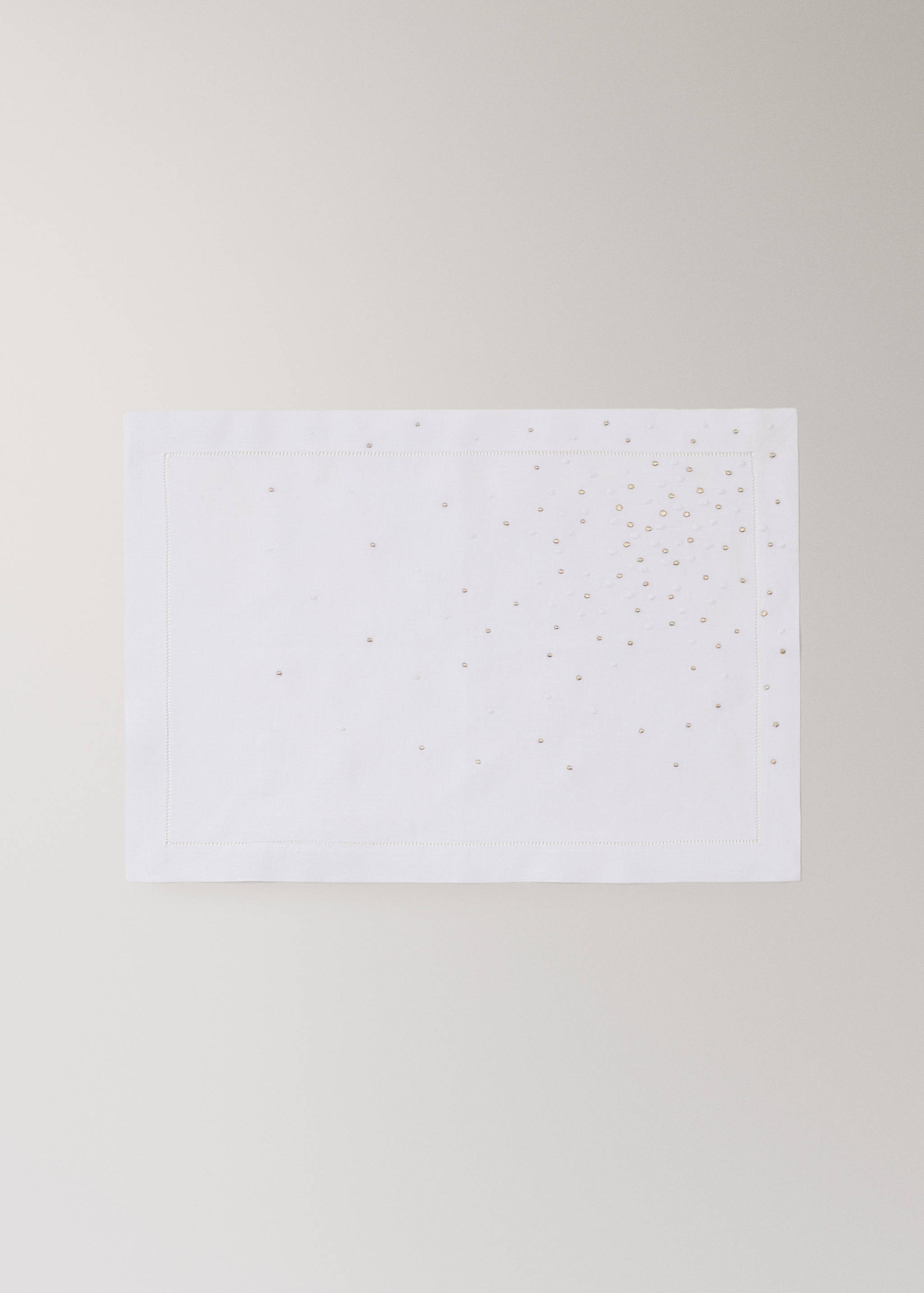 White rectangular placemat with a stitched border and scattered metallic beads.