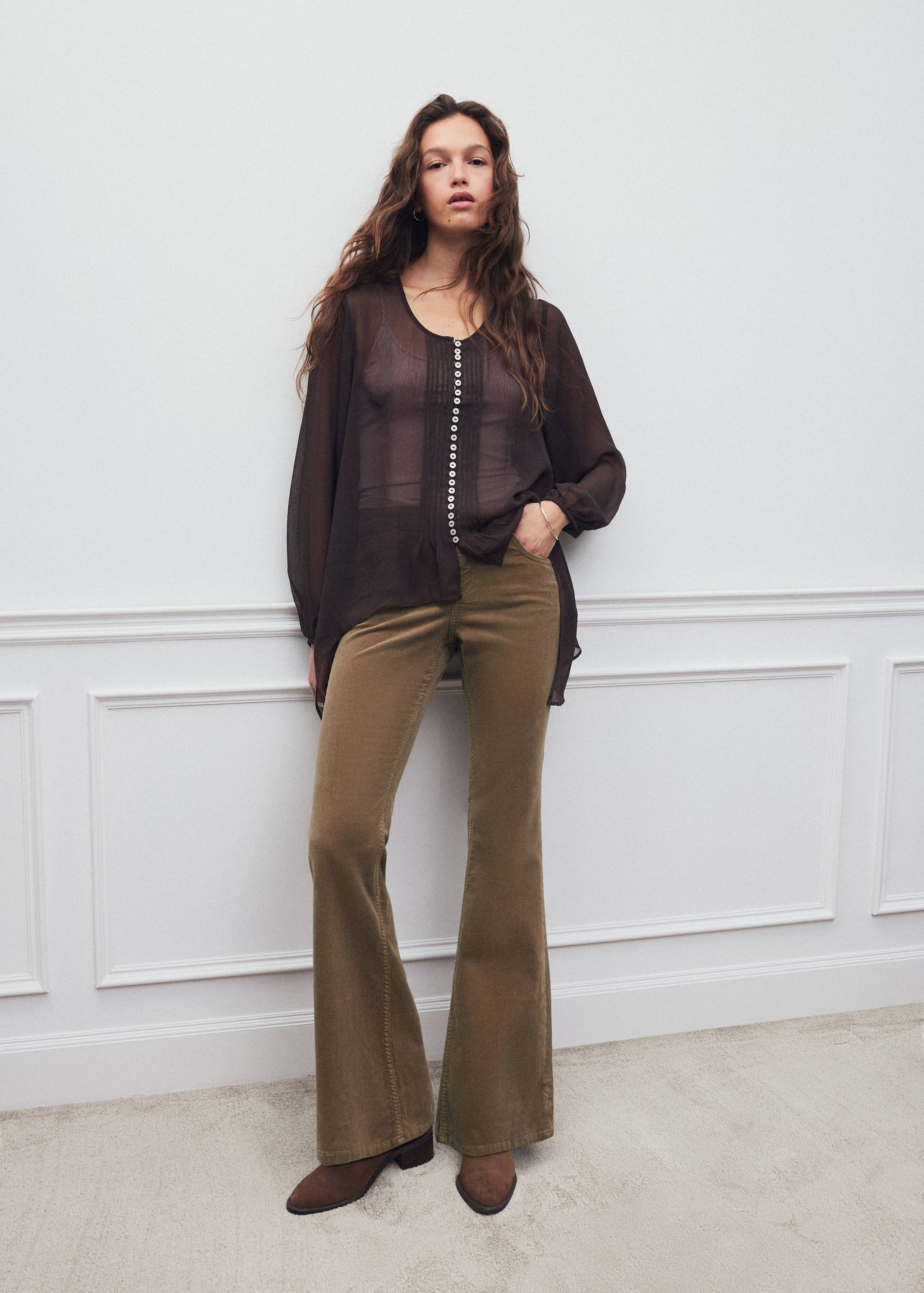 Olive green flared trousers worn with a dark brown sheer blouse.