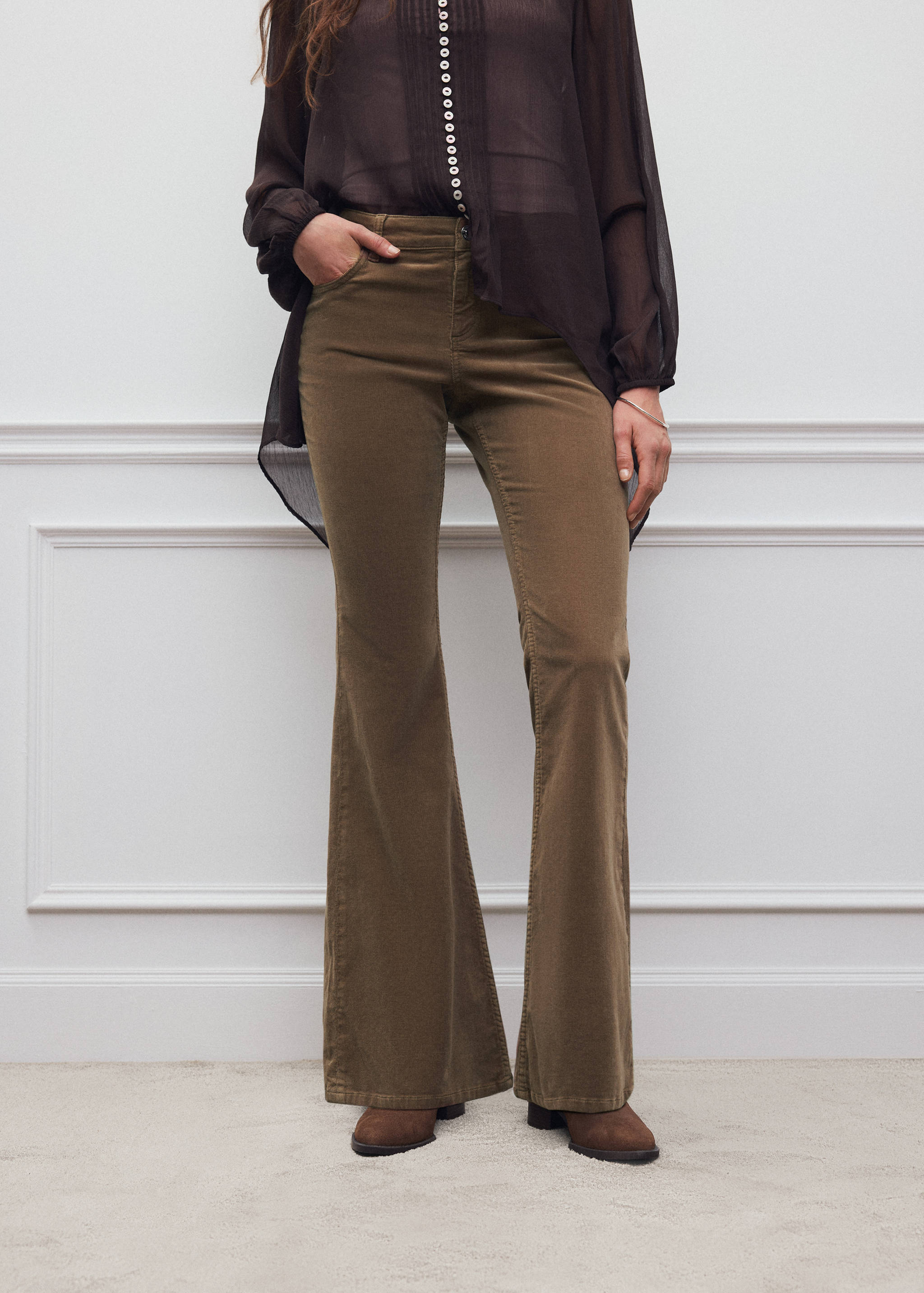 Dark olive green corduroy flared trousers worn with a dark sheer blouse.