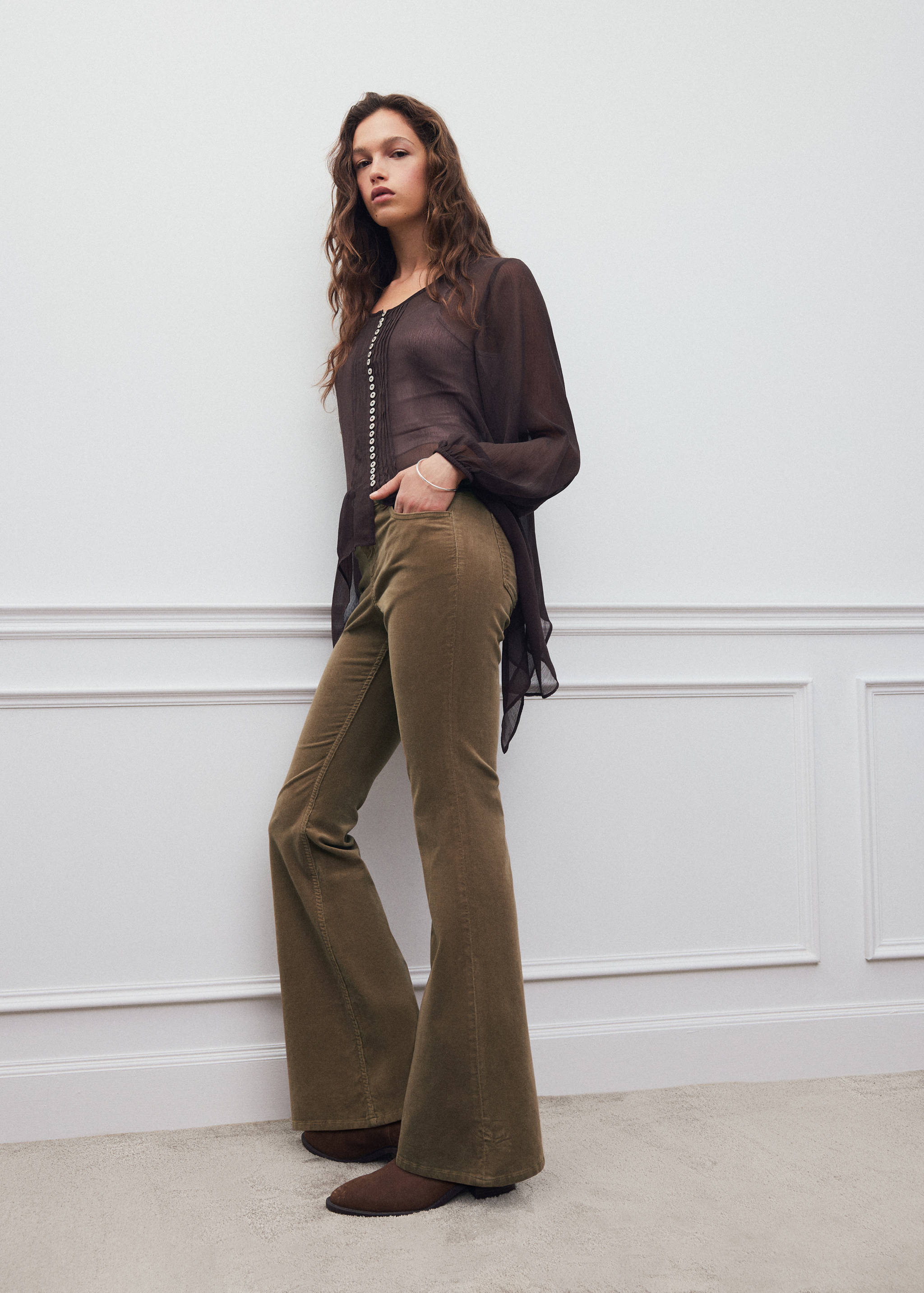 Olive green corduroy flared trousers worn with a sheer dark brown blouse.
