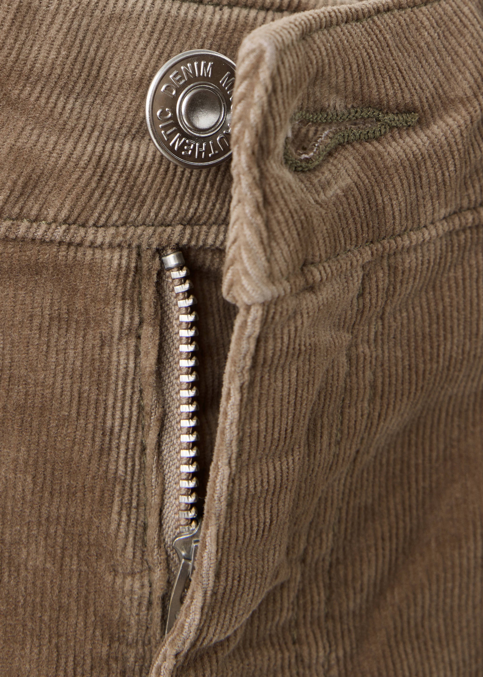 Close-up of brown corduroy trousers featuring a button and zip fly detail.