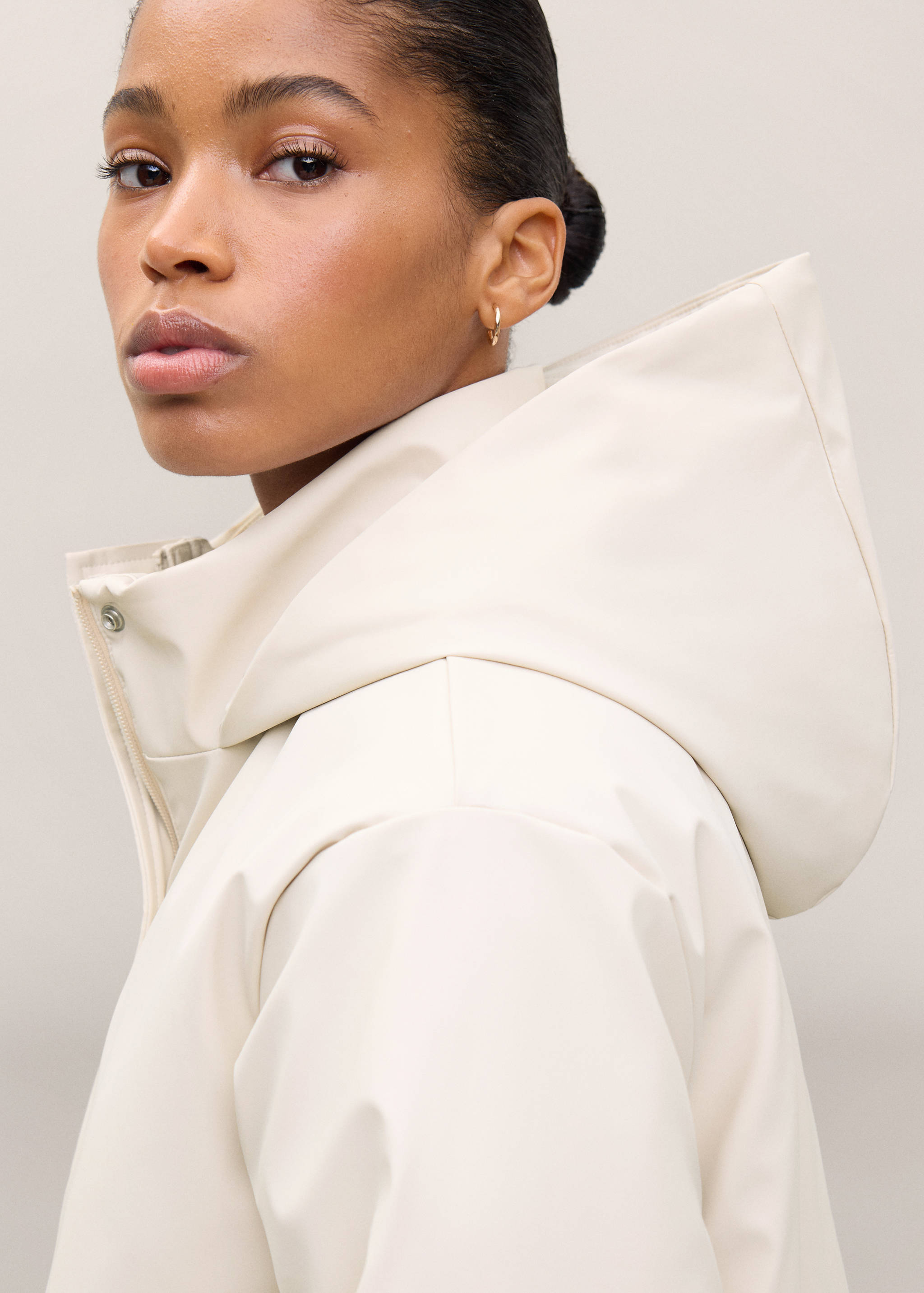 Primer plano de una chaqueta en color blanco roto con capucha estructurada y cuello alto.