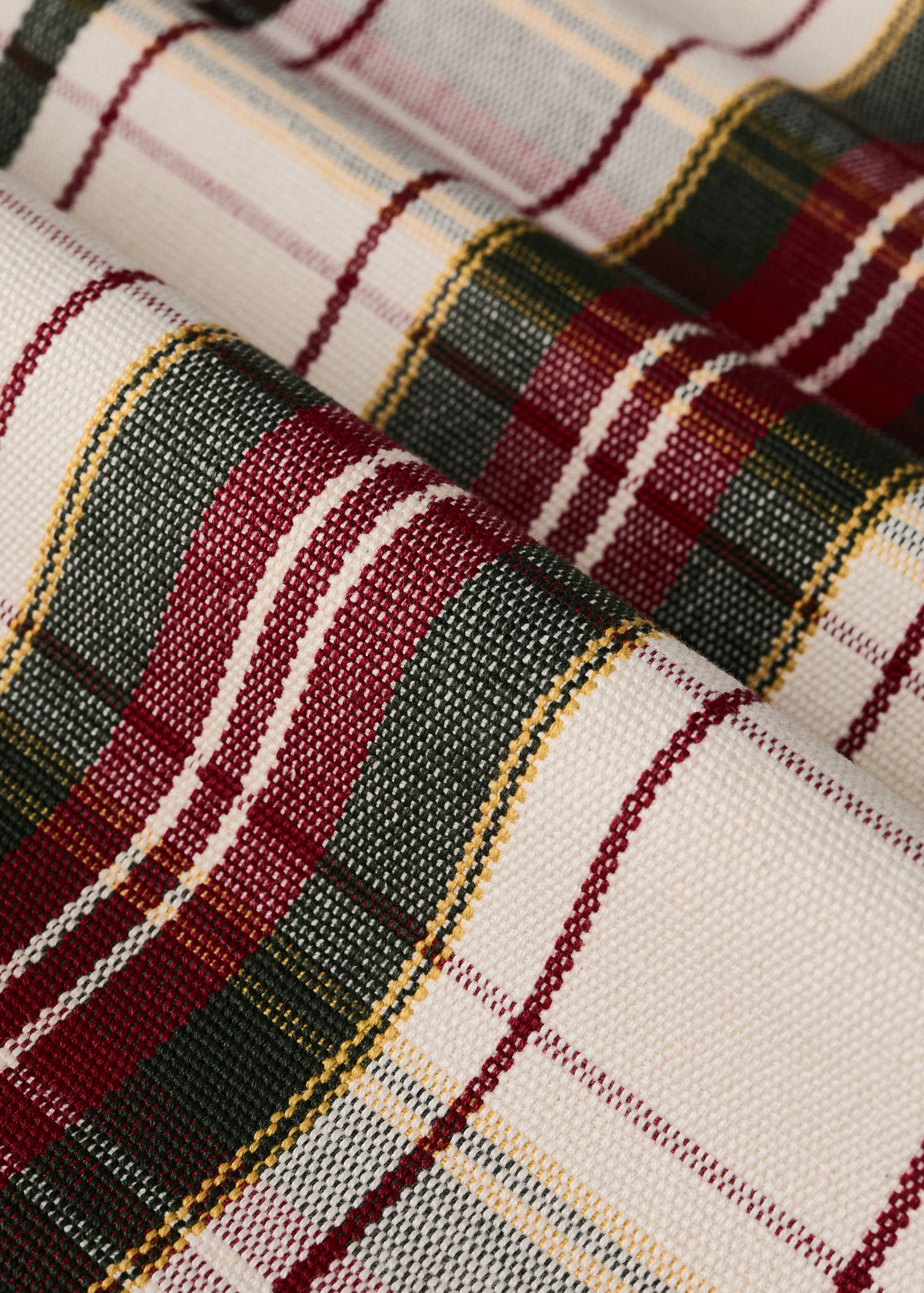 Close-up of a cream table runner with a red, dark green, and yellow tartan plaid pattern.