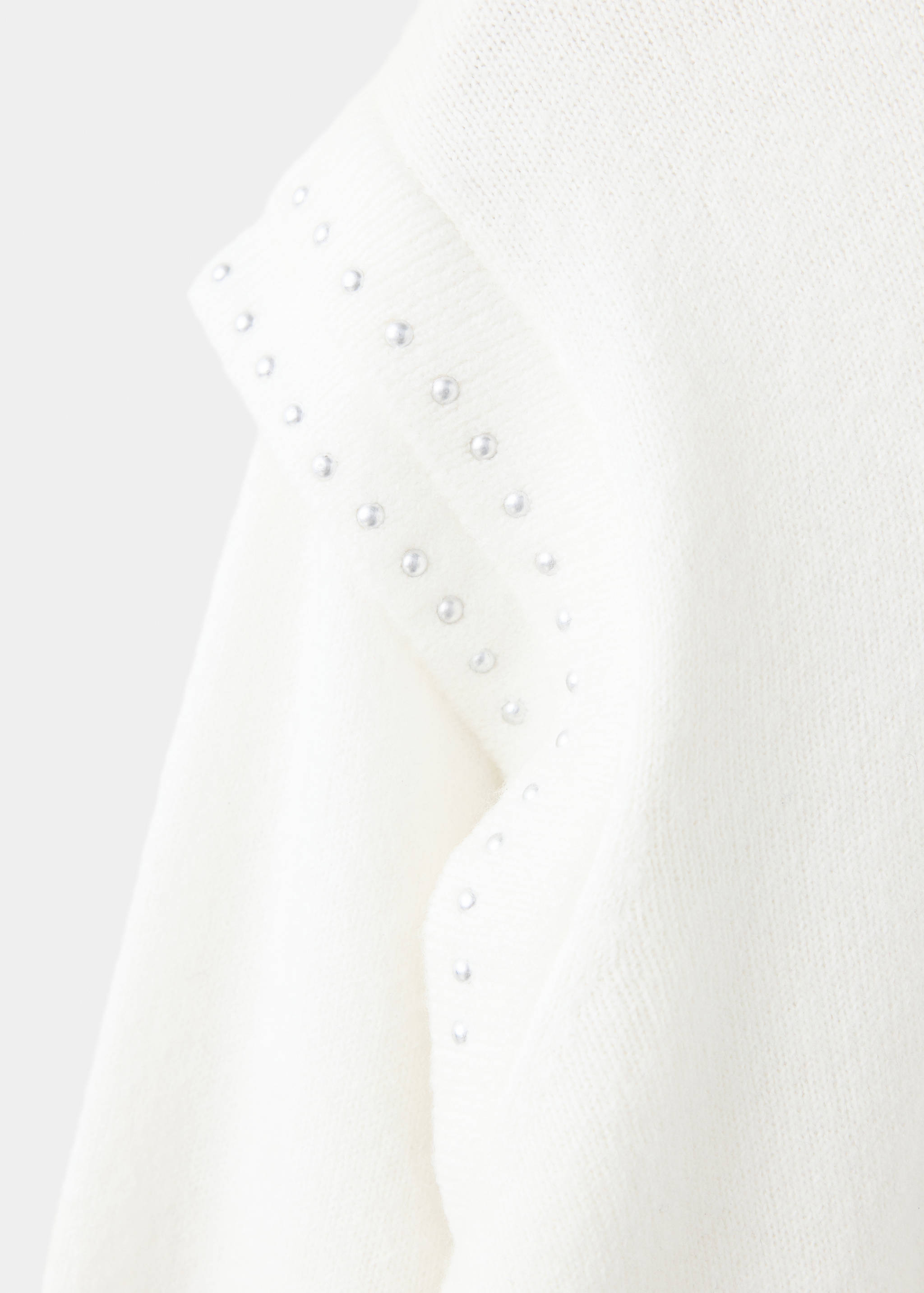 Close-up of a white knitted jersey with silver stud-embellished shoulder detail.