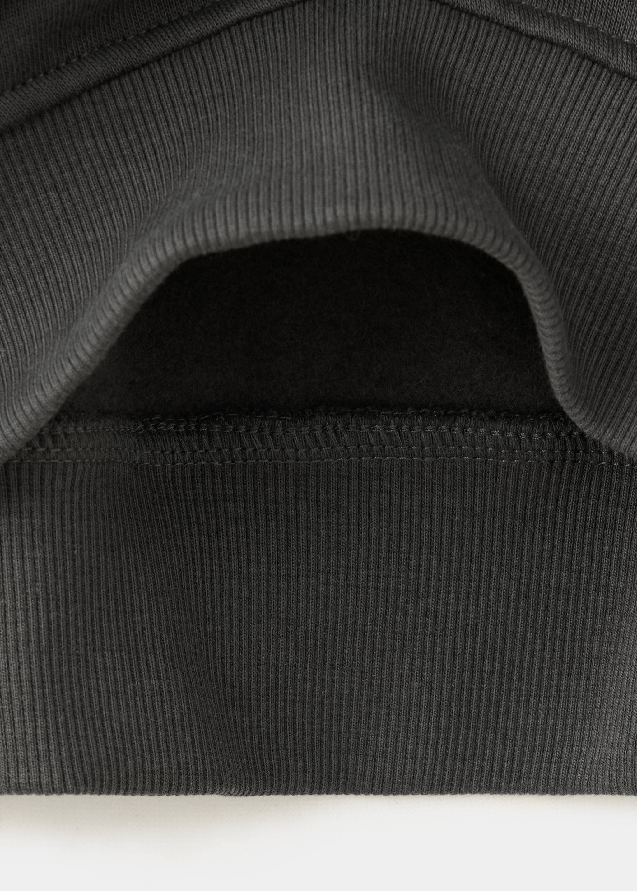 Primer plano de la textura del tejido y el dobladillo de canalé de una sudadera gris oscuro.