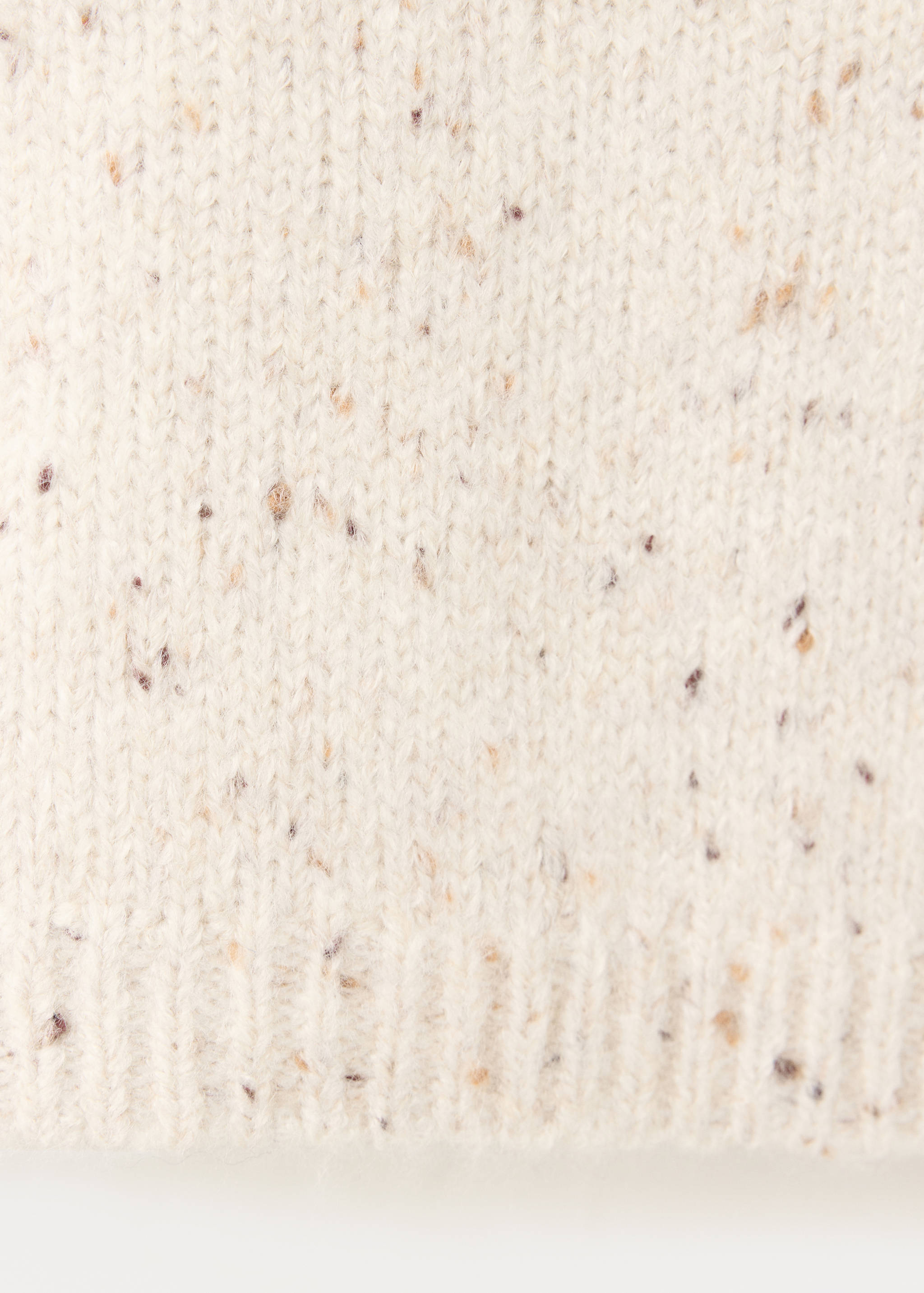 Close-up of an off-white speckled knit jersey fabric with a ribbed hem.