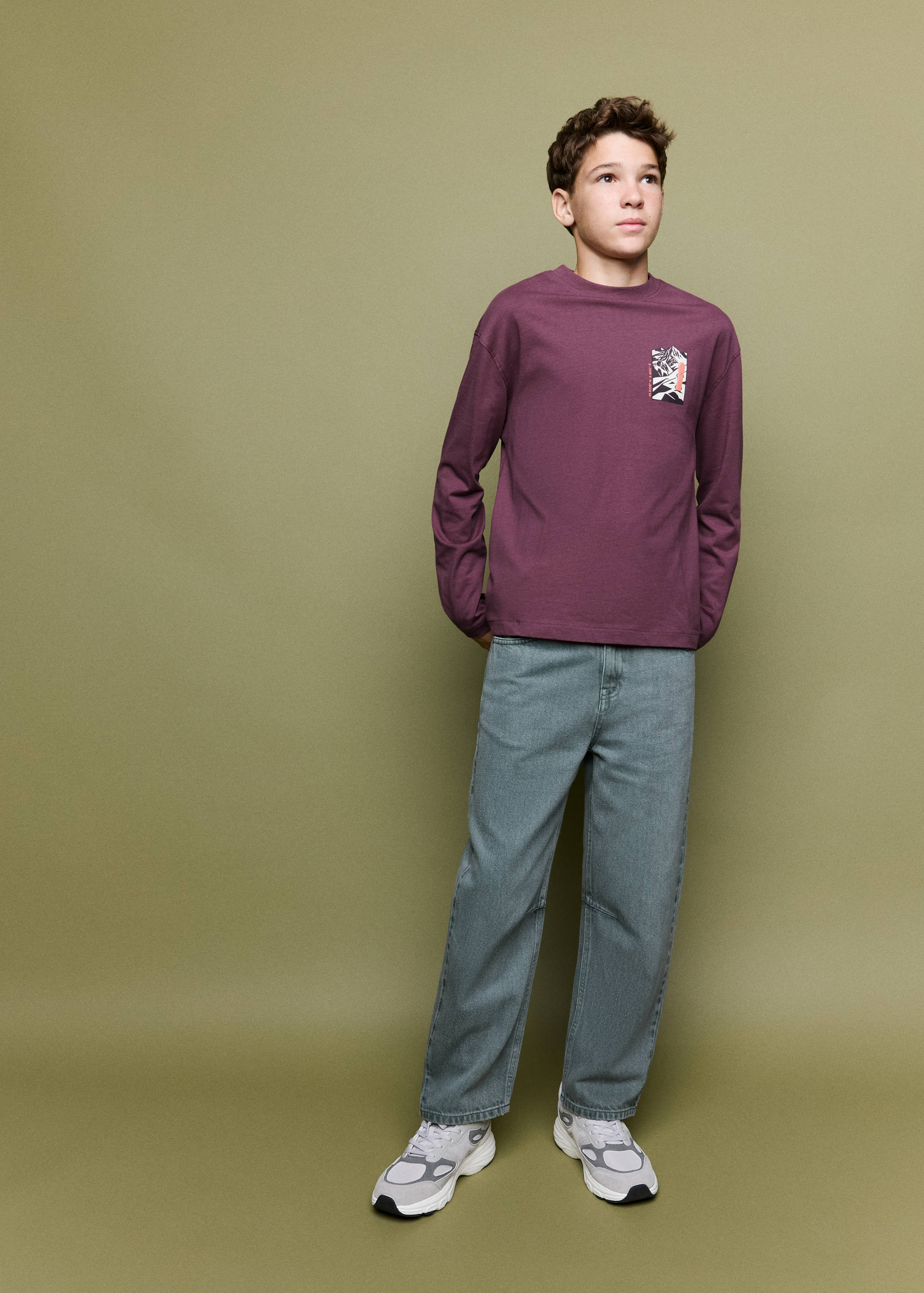 Plum-purple long-sleeved t-shirt with a small chest graphic, worn with denim trousers.