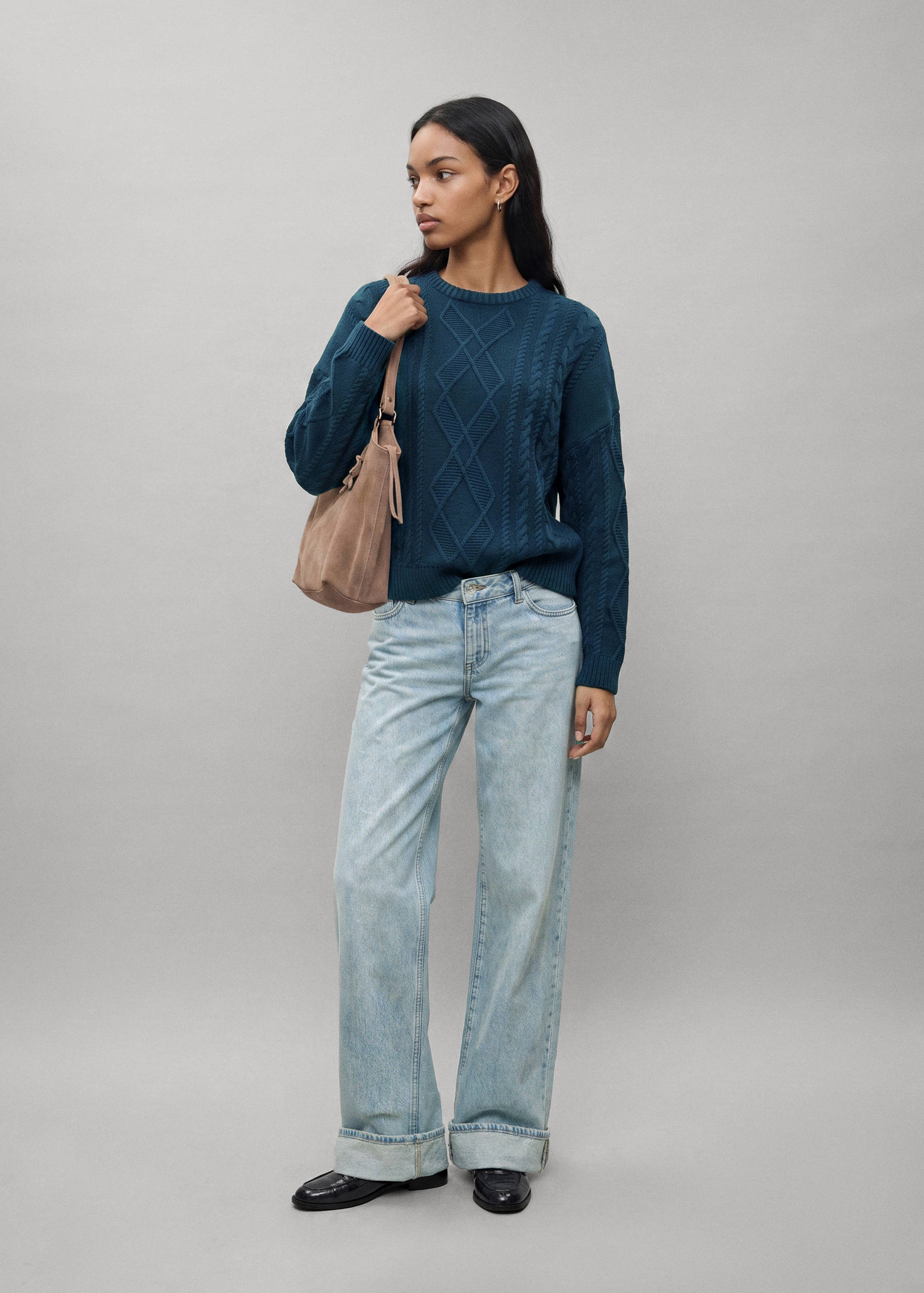 Dark teal cable-knit sweater with a crew neck, worn with light blue cuffed jeans.